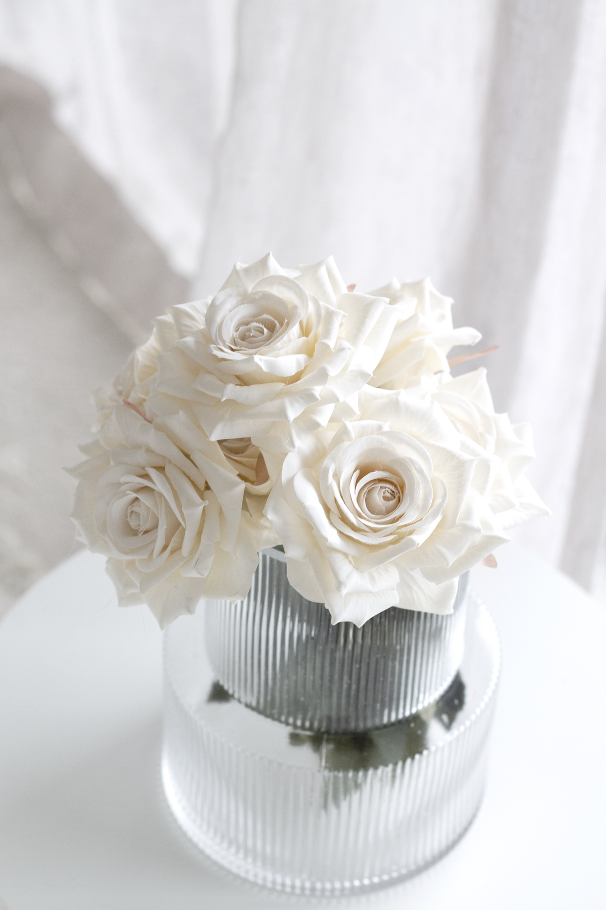 Champagne roses in a ribbed glass vase in front of sheer curtains
