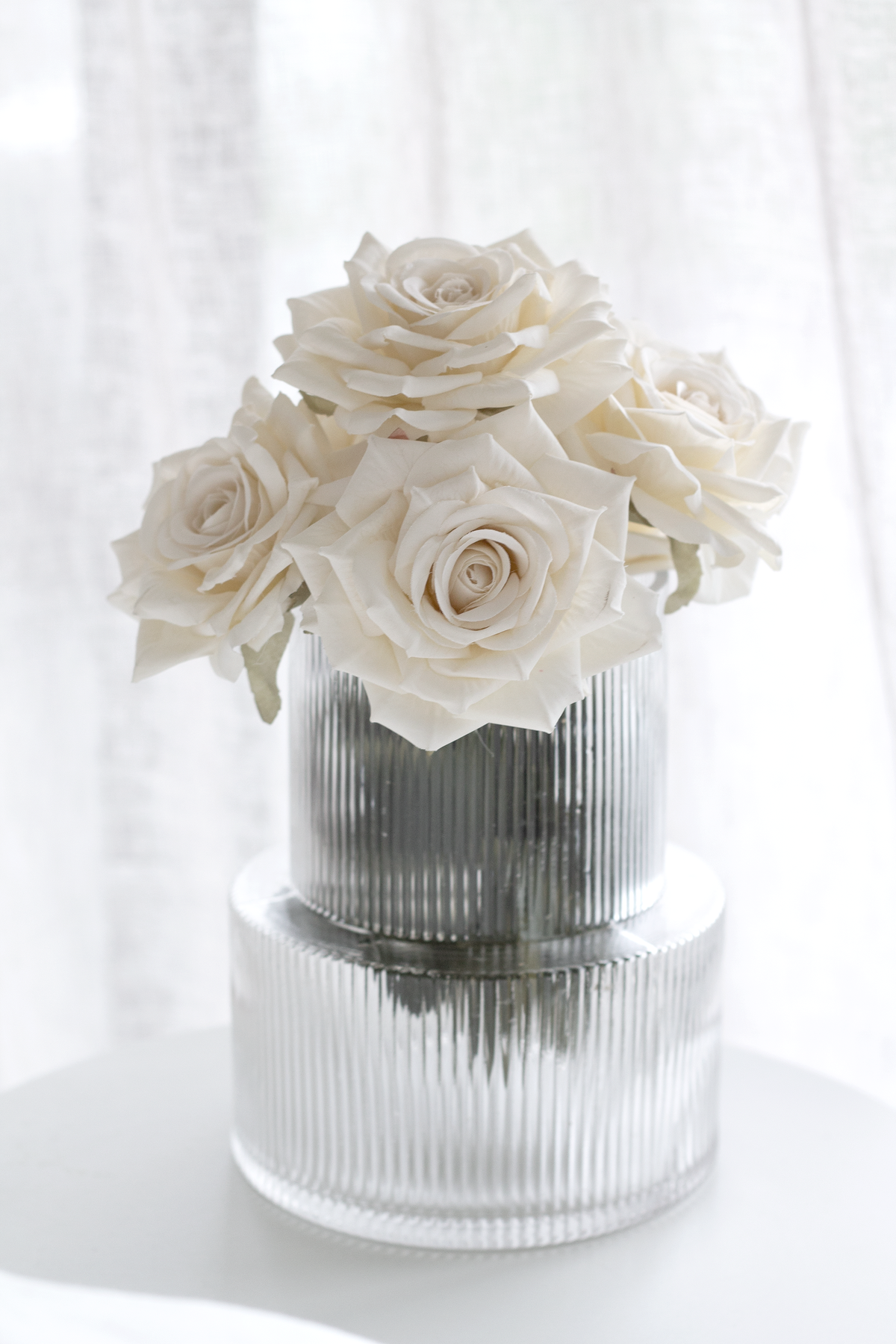 Ribbed glass vase filled with cream roses, styled on a white pedestal table