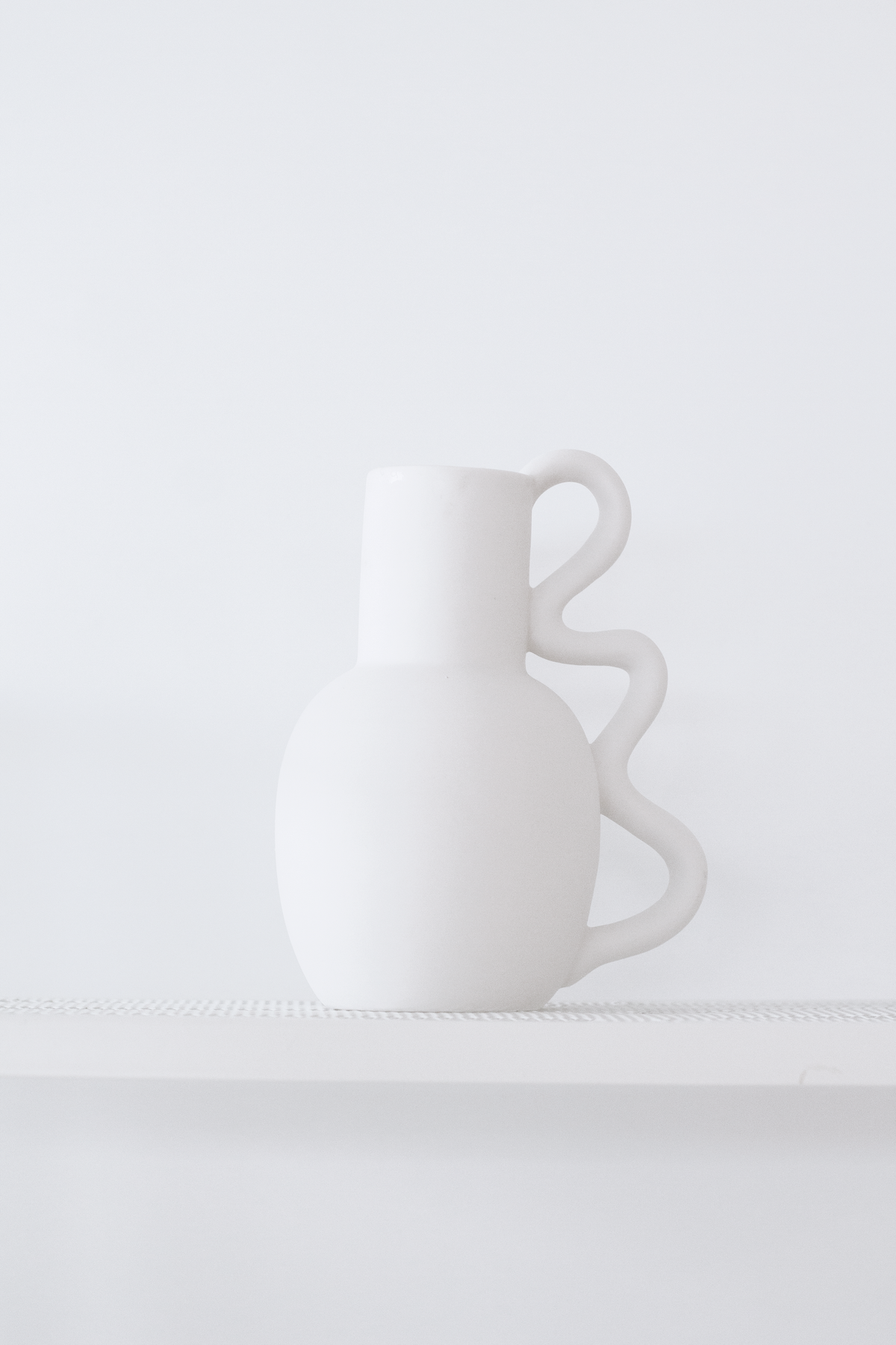 Empty Chloe vase on a white ledge against a pale grey wall