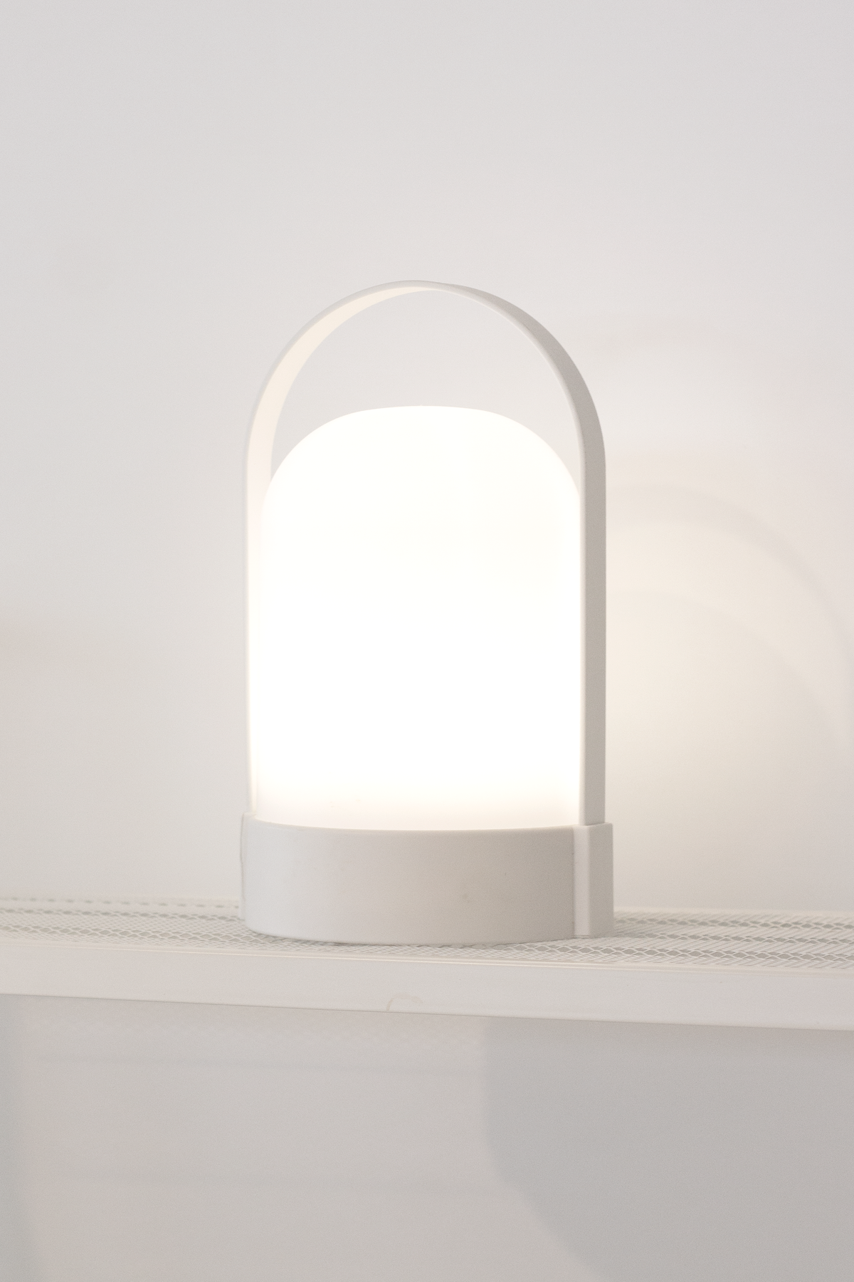 White portable LED lamp glowing on a shelf against a pale wall