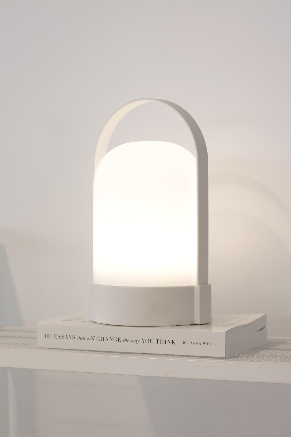 White portable LED lamp glowing on a stack of books beside a pale wall