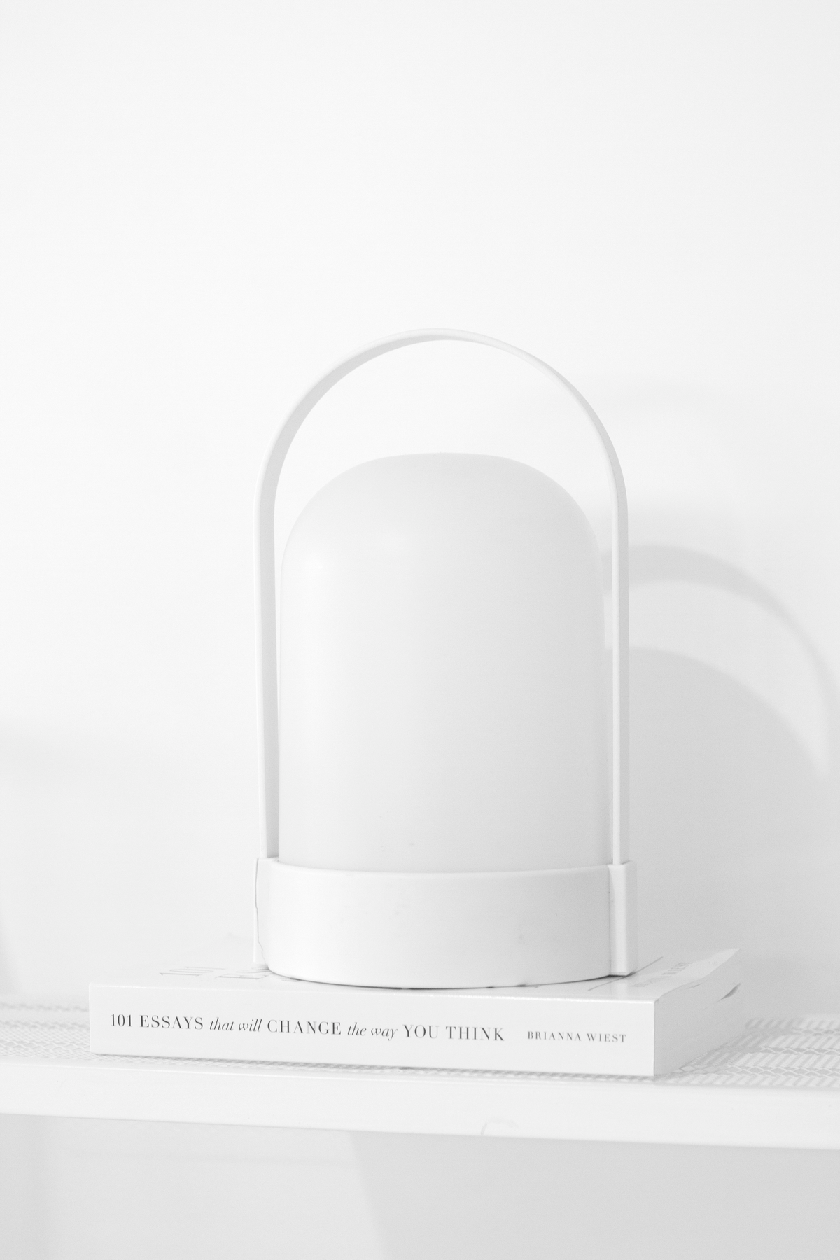 White portable LED lamp switched off, resting on a stack of white books against a pale wall
