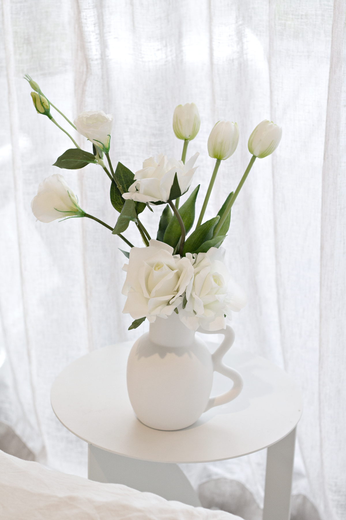 Chloe vase of white tulips on a round table beside a sheer curtain
