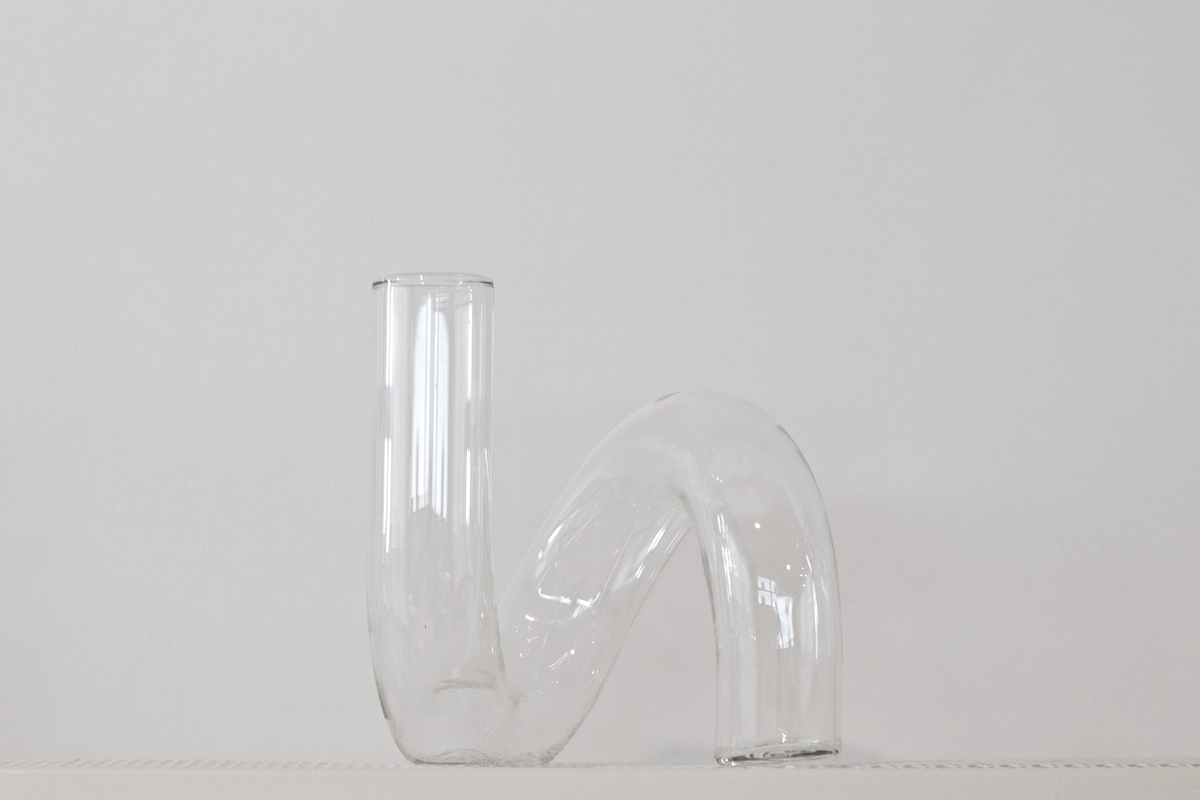 Clear J-Curve vase side on, showing the open neck and curled base against pale grey