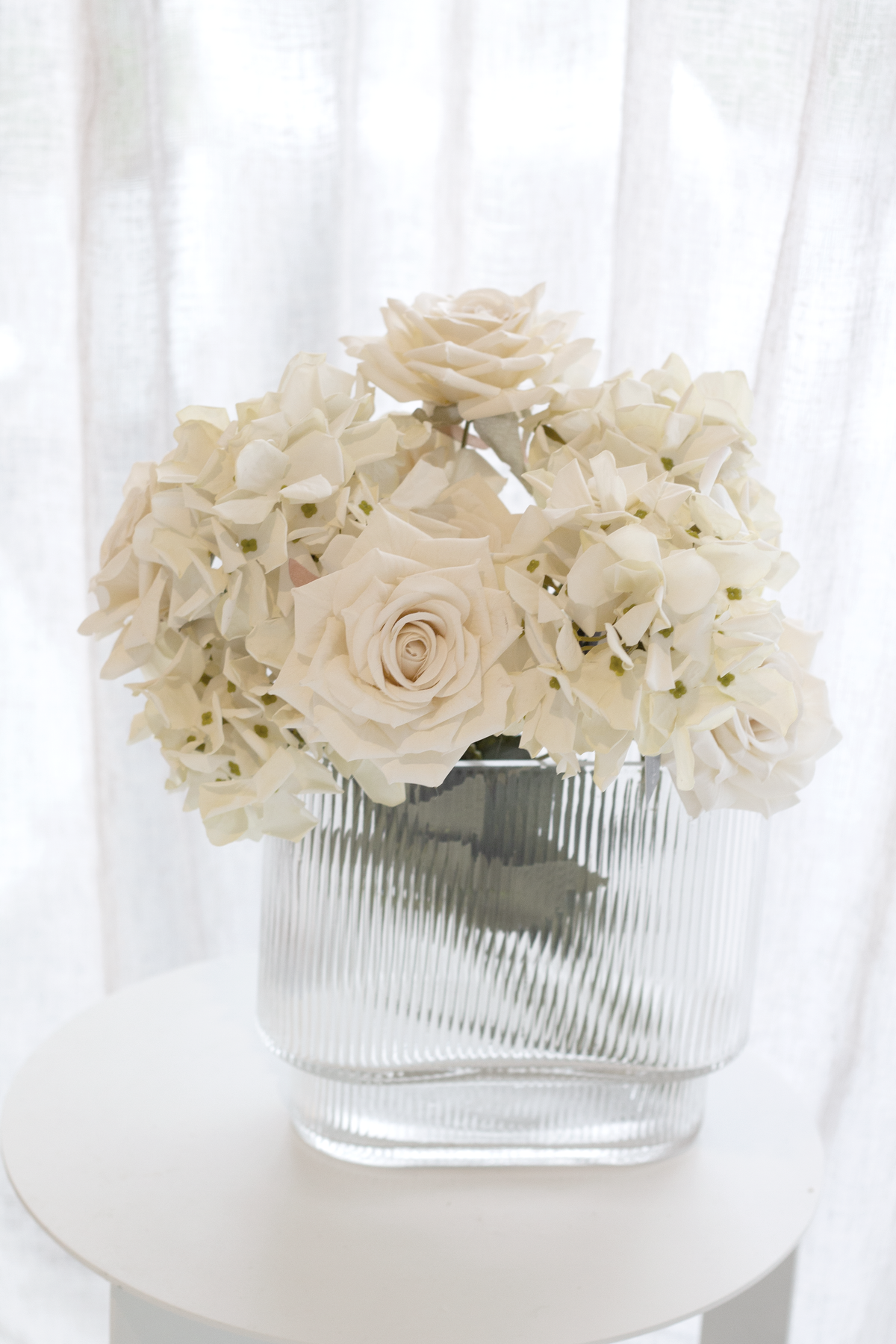Champagne faux roses in a ribbed glass vase on a white table