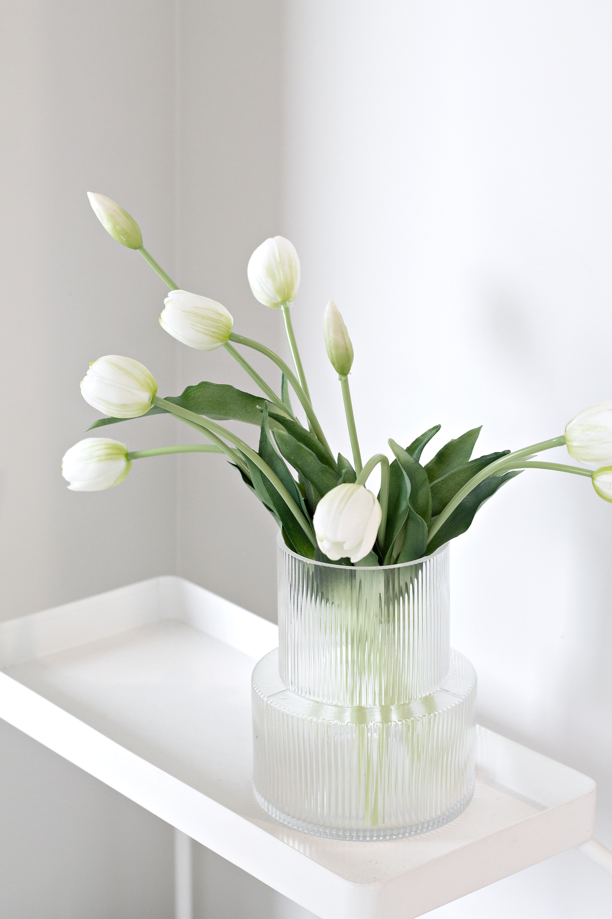 White tulips arranged in the clear ribbed vase on a white tray topped console