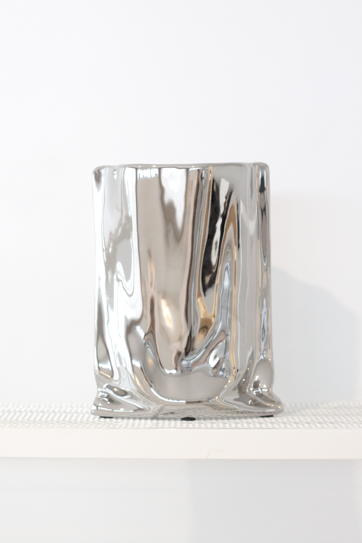 Silver metallic bag vase on a white ledge, pale grey backdrop