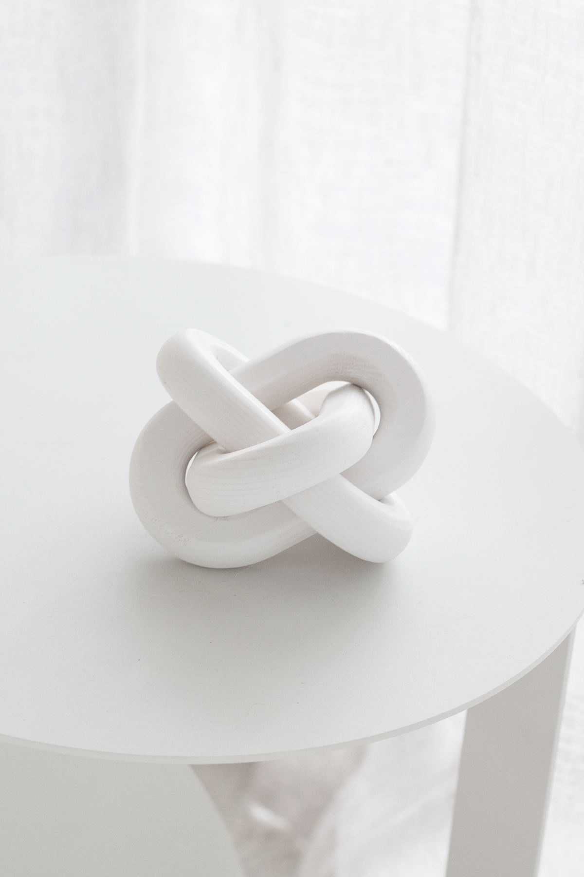 White knot ornament on a round white side table with a sheer curtain behind