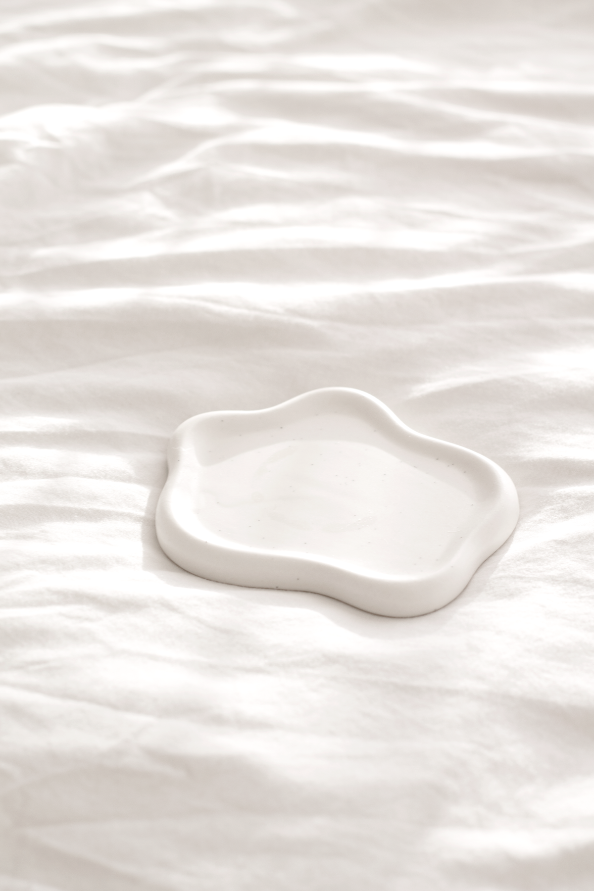 Empty white cloud trinket dish resting on white linen