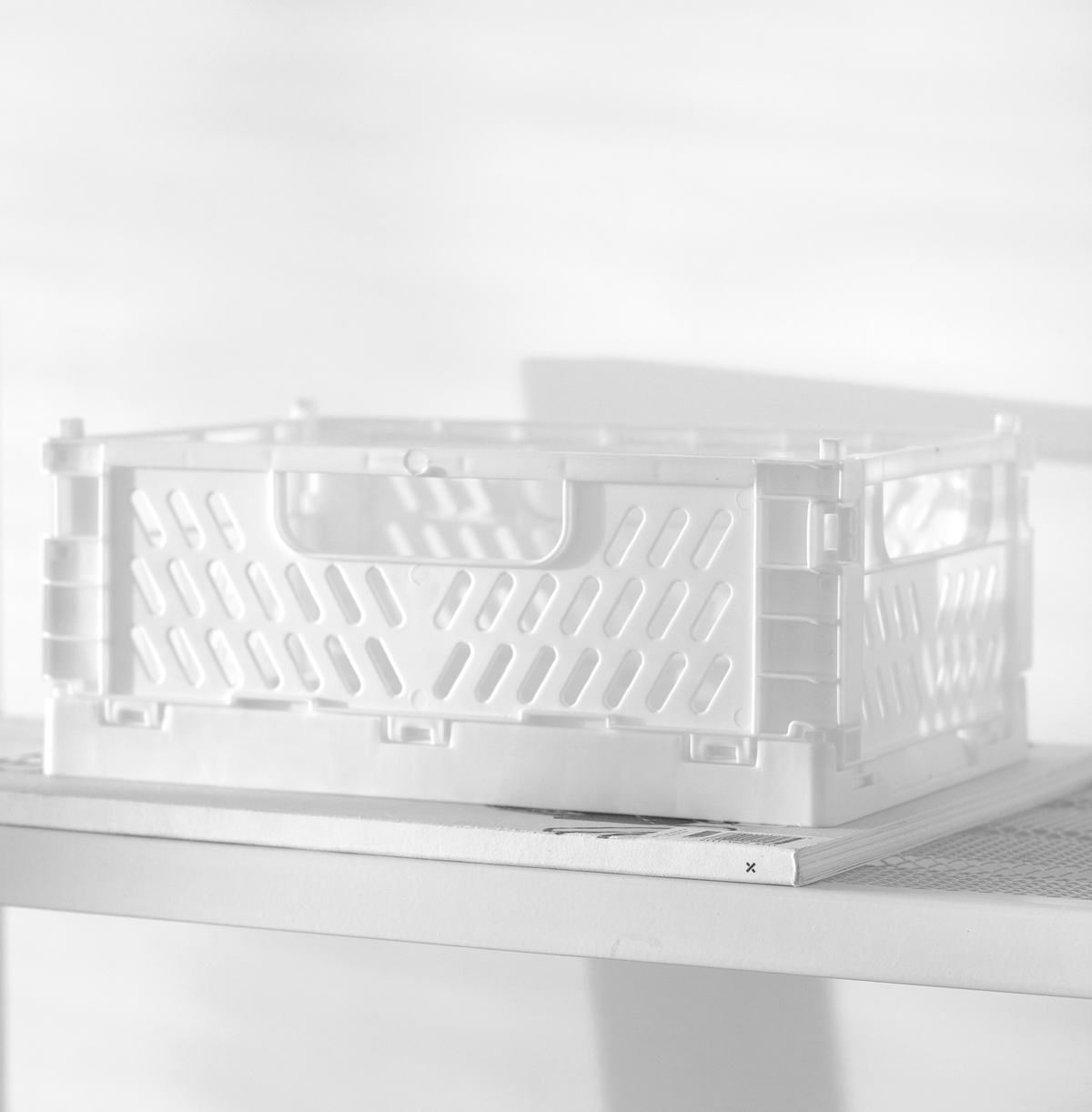 White crate sitting on a pale shelf in soft daylight, slotted sides in profile