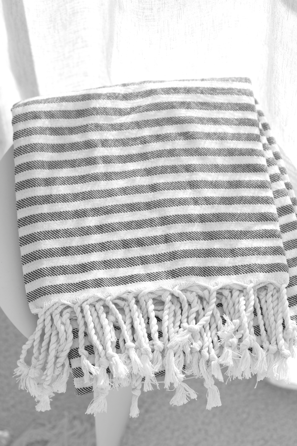 Grey striped Turkish towel folded over a chair by a window with a sheer curtain