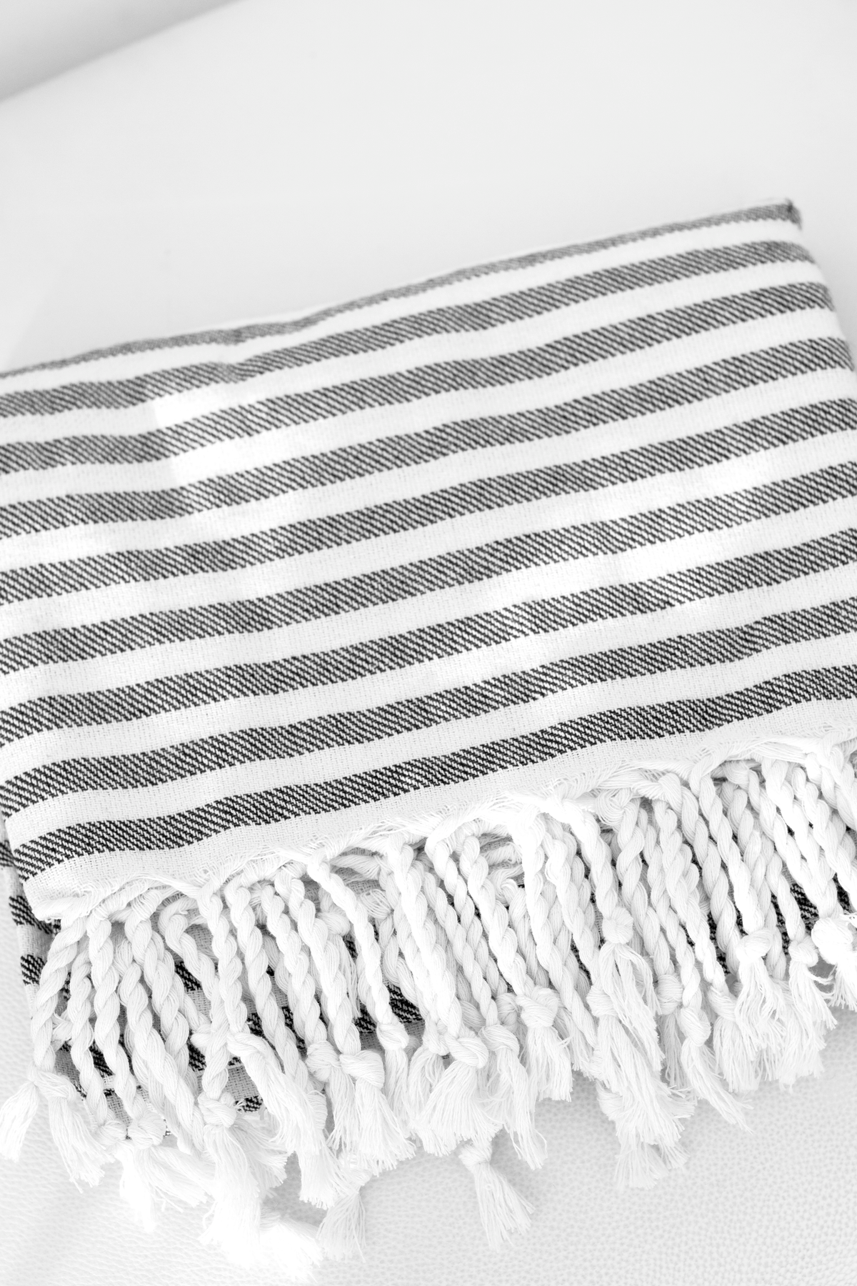 Grey striped Turkish towel folded on a pale surface, showing the knotted tassel fringe
