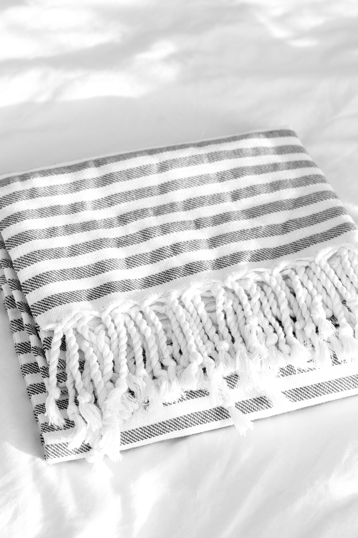 Grey striped Turkish towel folded on white bedding with the fringe facing out