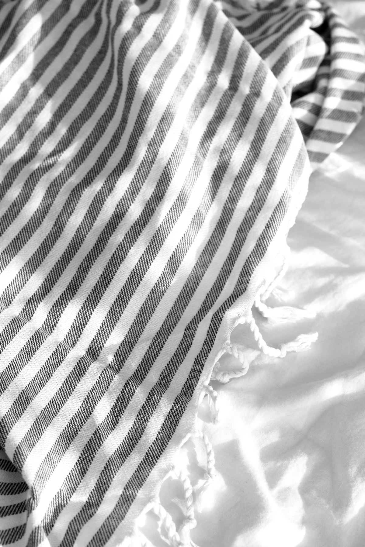 Close up of the grey striped Turkish towel draped over white bed linen