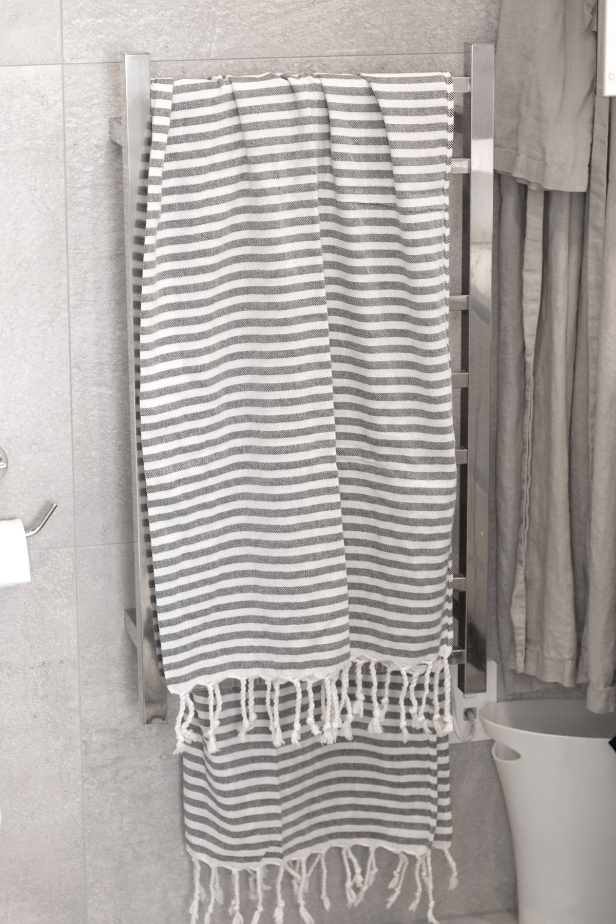 Grey striped Turkish towel hanging on a bathroom rail beside a shower curtain