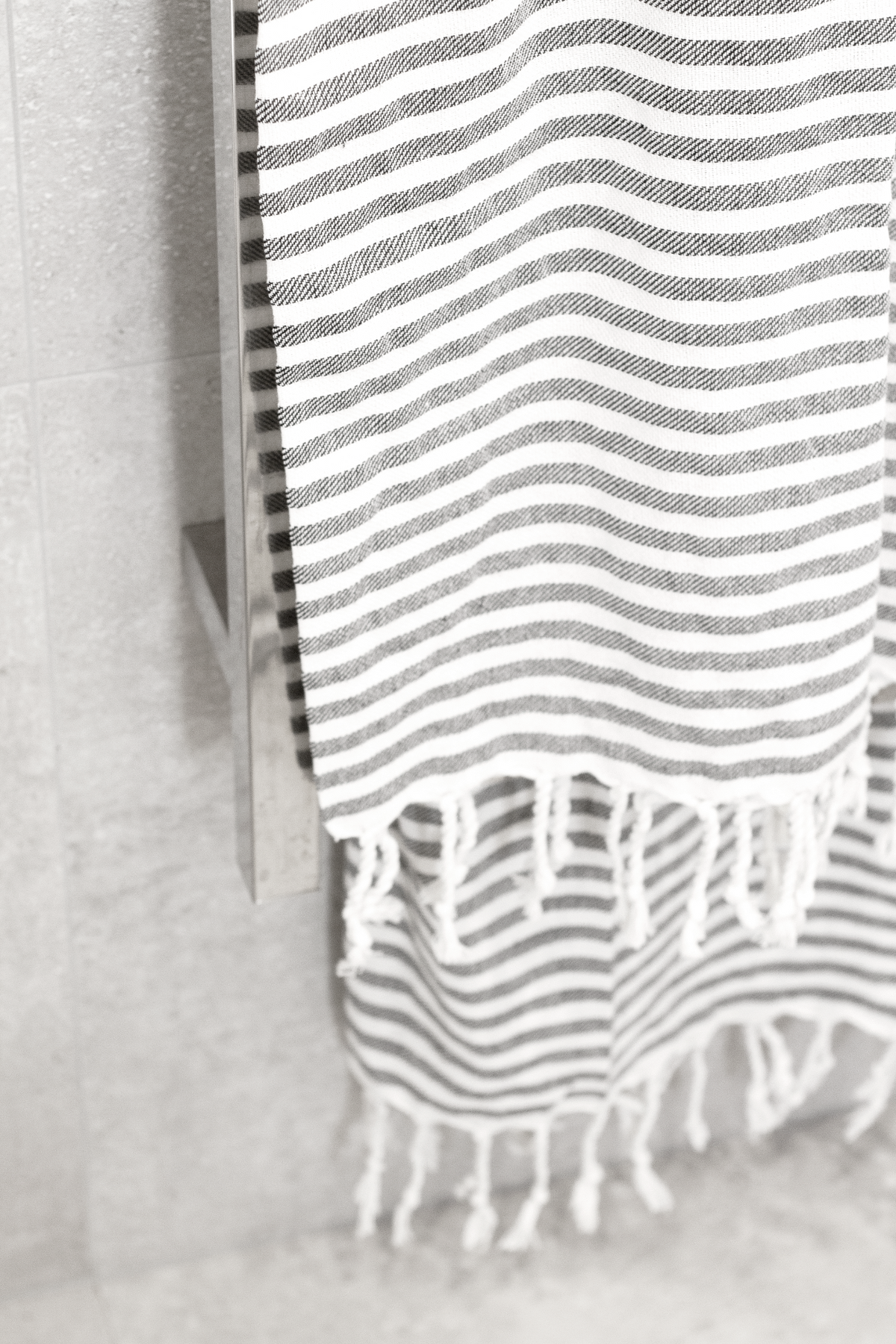 Grey striped Turkish towel hanging from a rail against a concrete wall