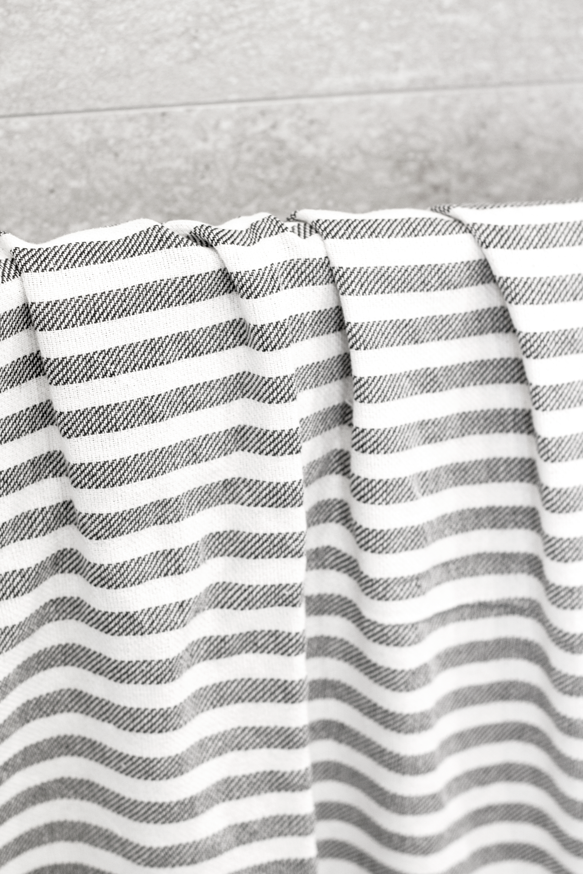 Grey striped Turkish towel hanging in folds against a tiled wall