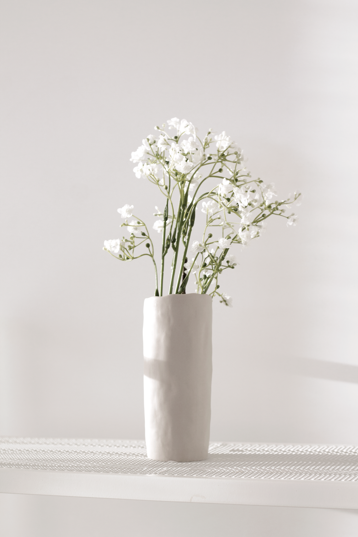 Faux gypsophila stems in a small white vase on a shelf