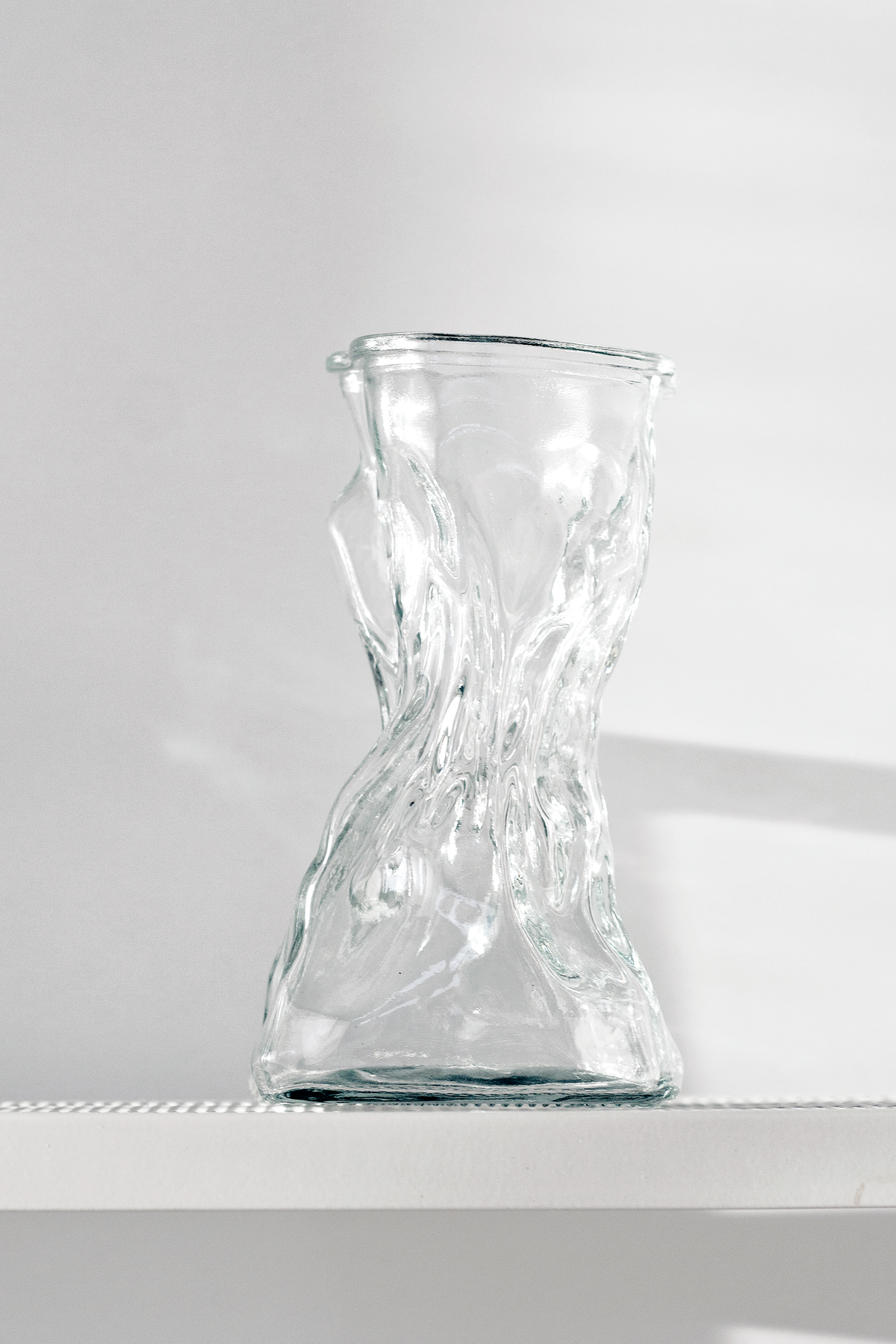 Clear crinkle vase on a white ledge against grey, its shadow falling to one side