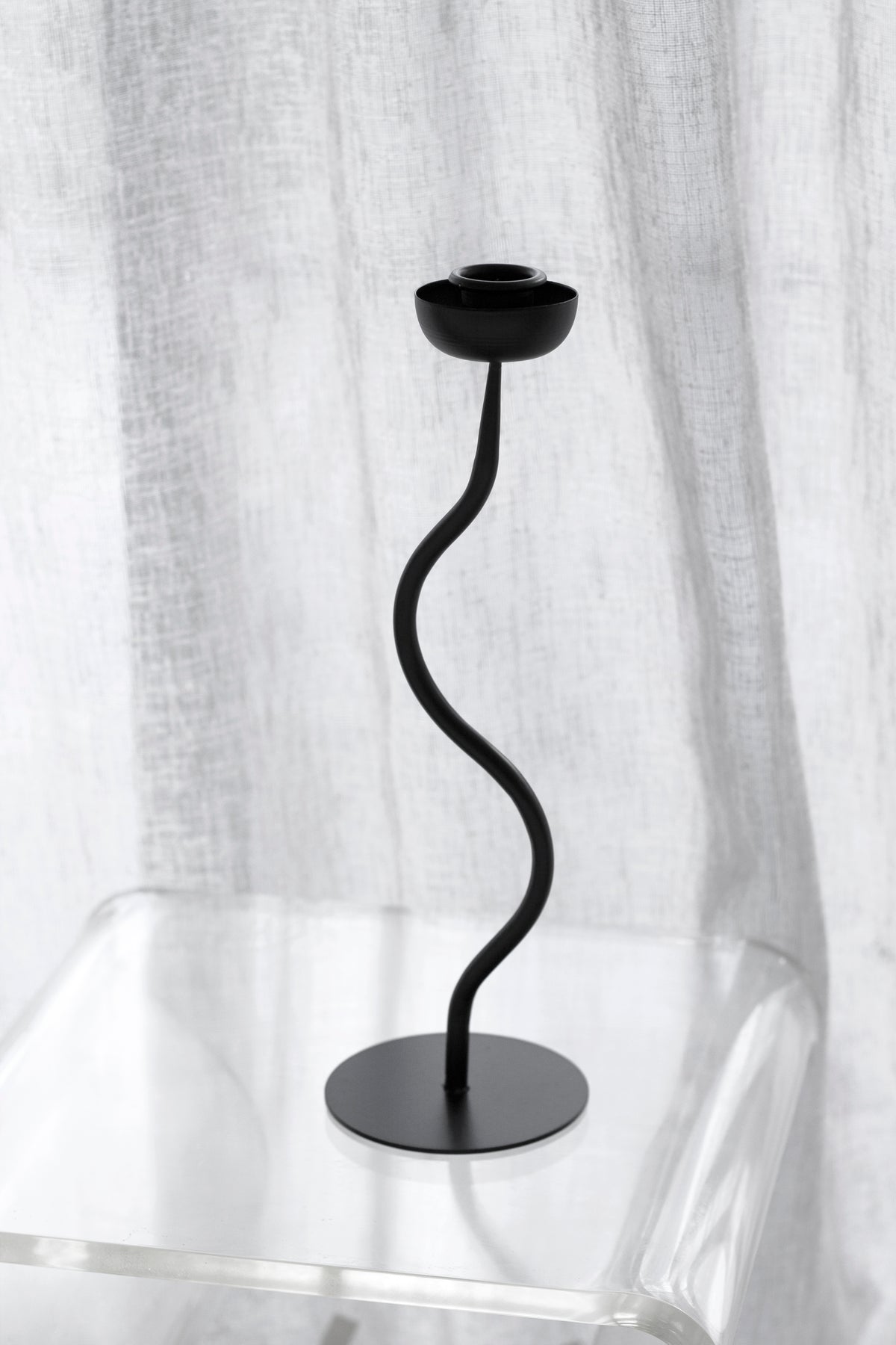 Aries candle holder on a clear acrylic side table with linen hanging behind