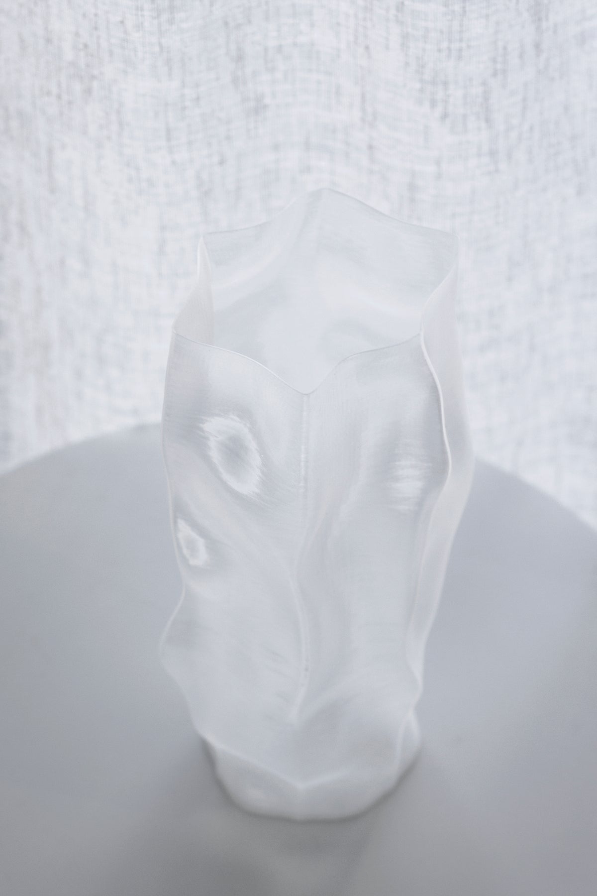 Close view of the transparent white vase, the rippled surface catching light from a window