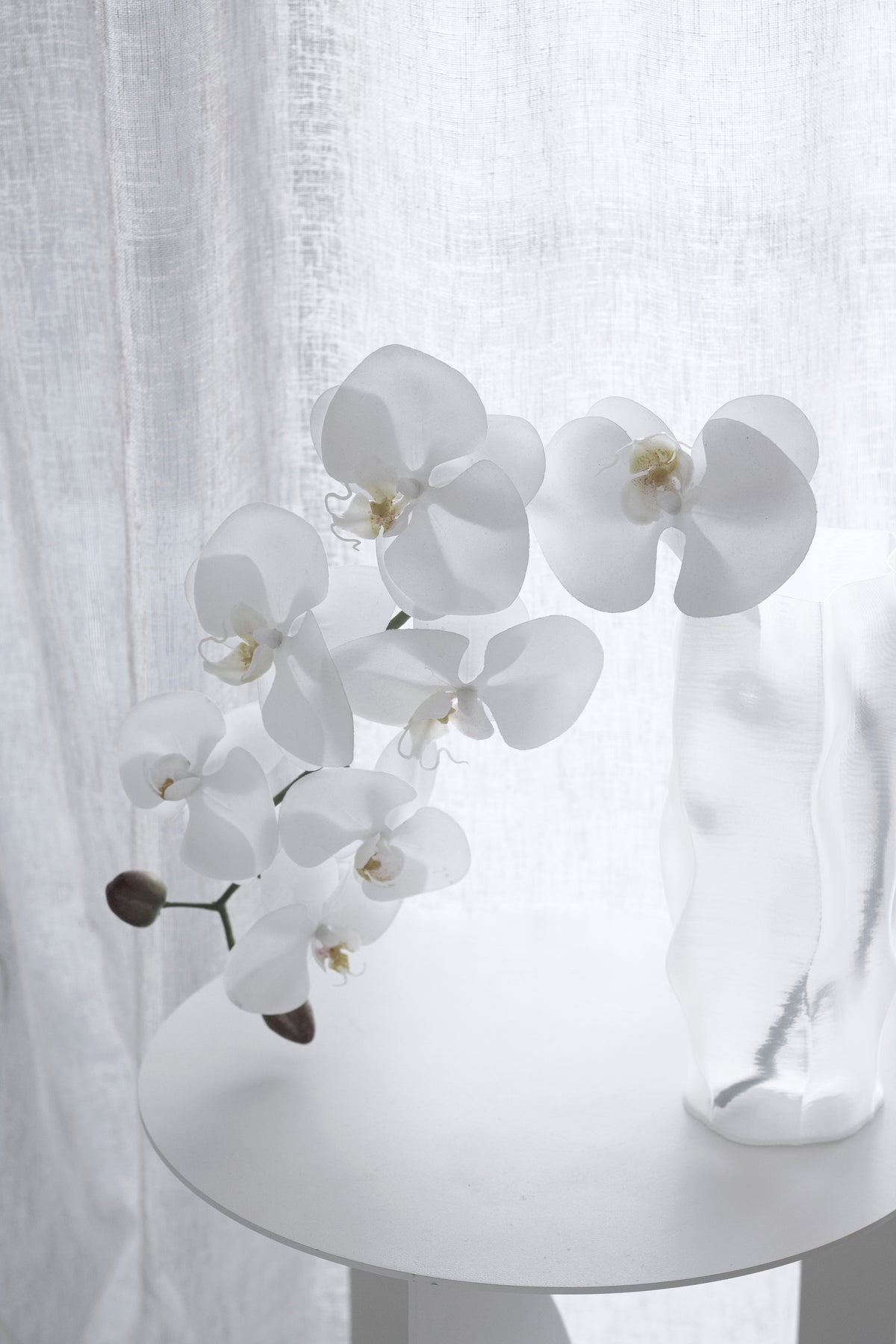 White orchid stems arching out of the ripple vase on a round grey table