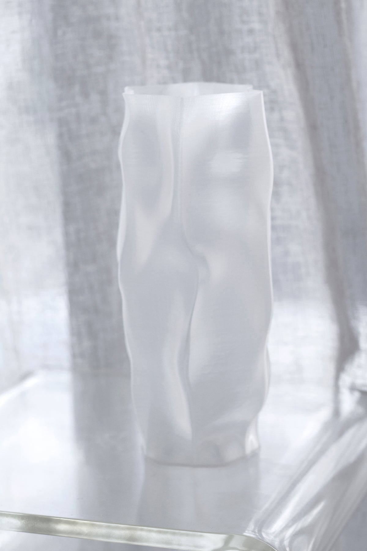 Three quarter view of the ripple vase on a glass table with a sheer curtain behind