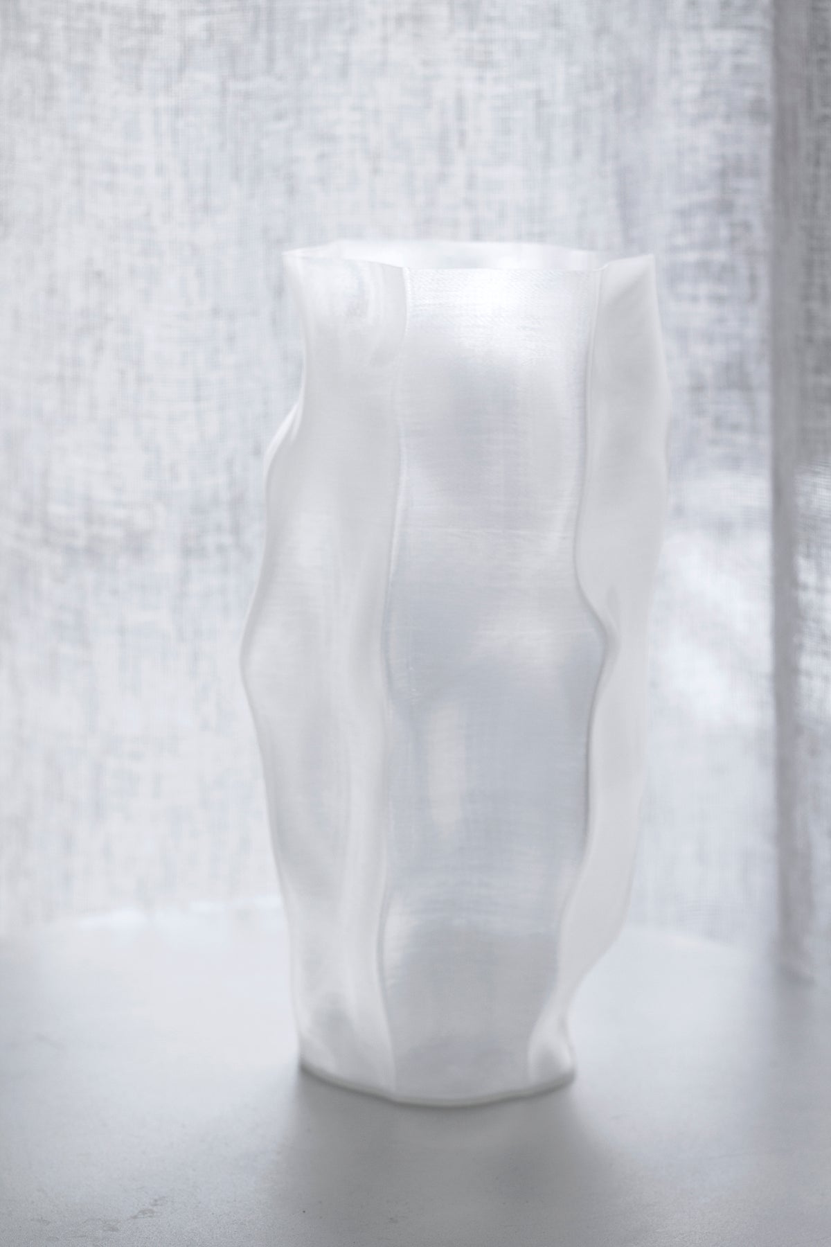 Ripple vase on a pale surface with sunlight falling across a linen curtain behind