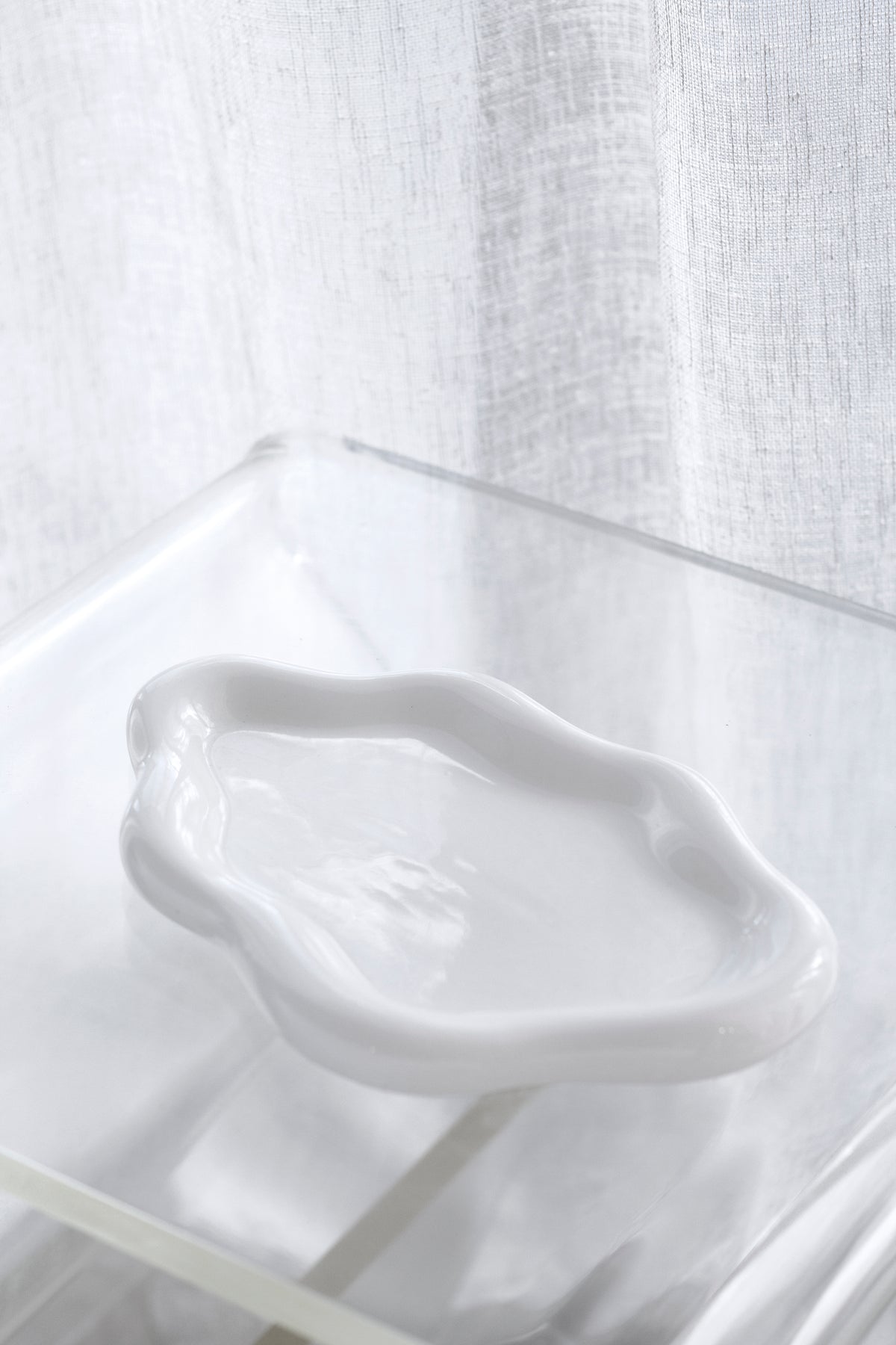 Empty white cloud ceramic tray on a clear acrylic surface, showing the wavy rim