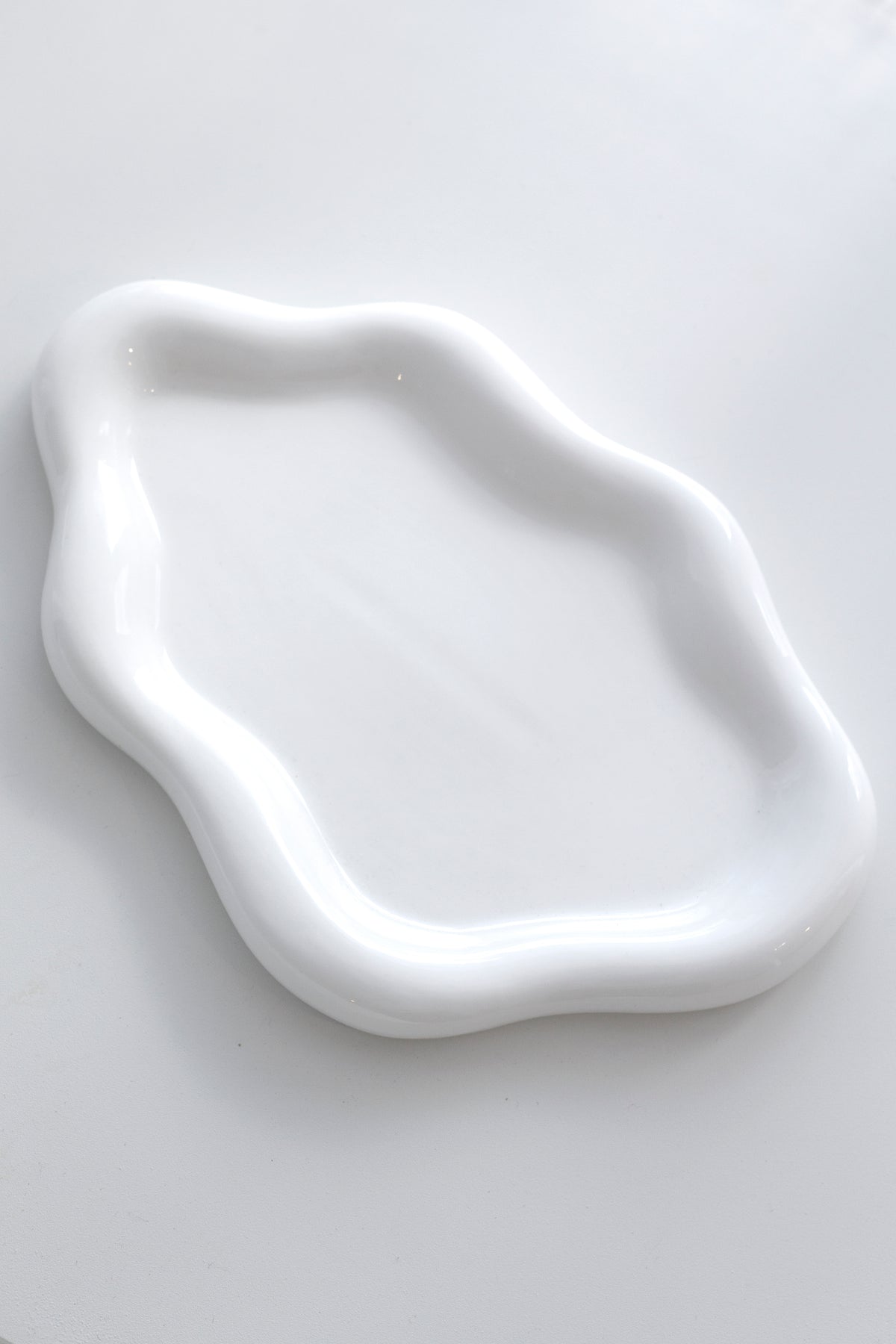 Empty white cloud ceramic tray on a soft grey surface, showing the wavy edge