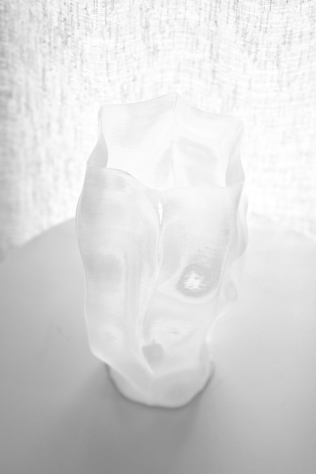 Ripple vase tilted towards the camera on a pale table, textured linen filling the background