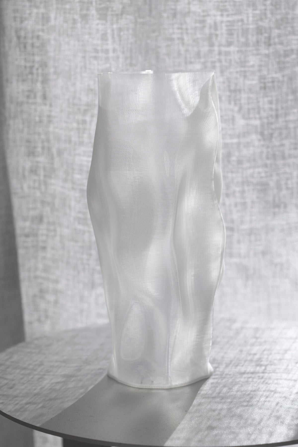 Ripple vase on a glass topped table, its folds silhouetted against woven linen