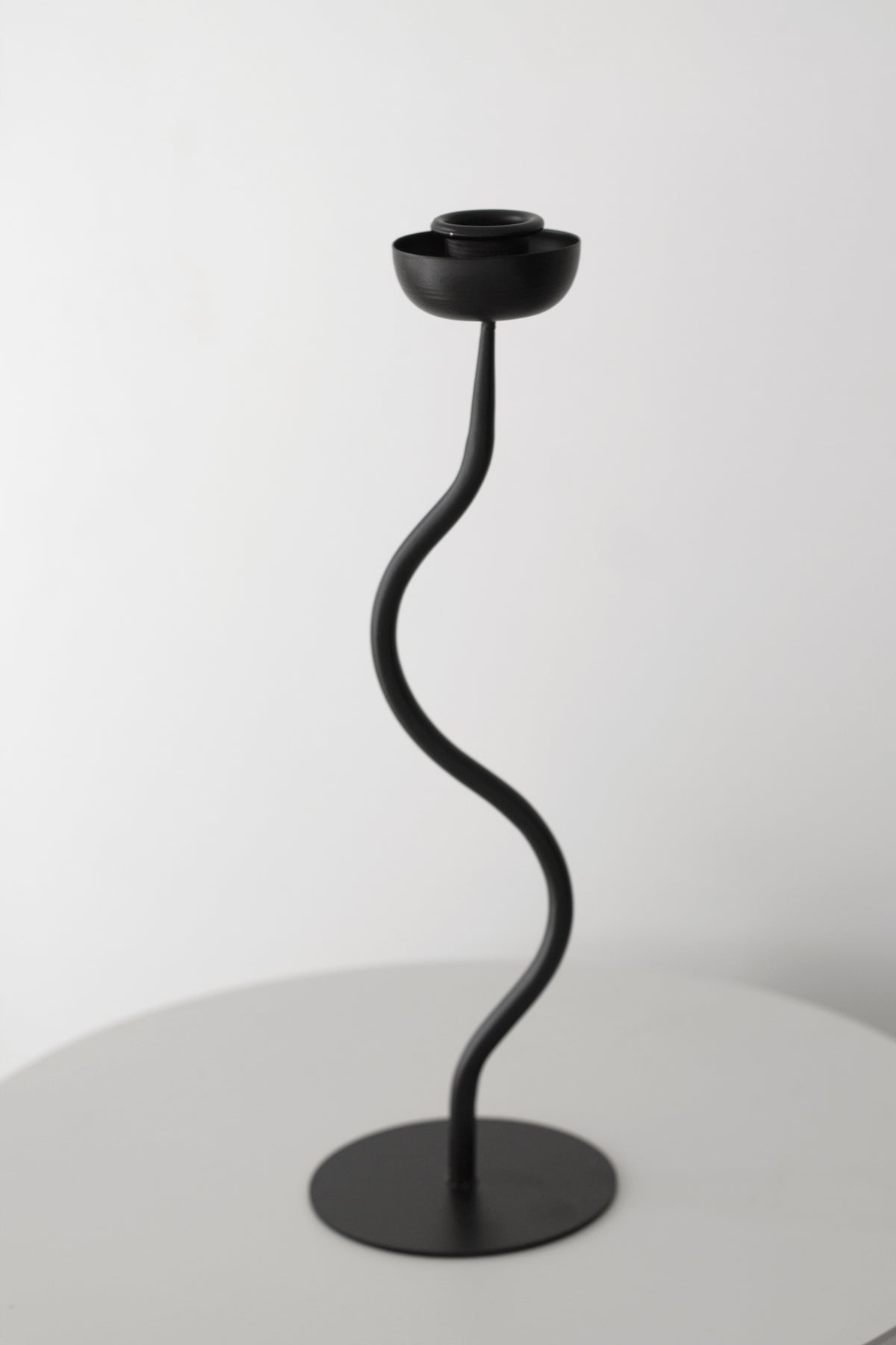 Black wavy candle holder alone on a pale table against a plain wall