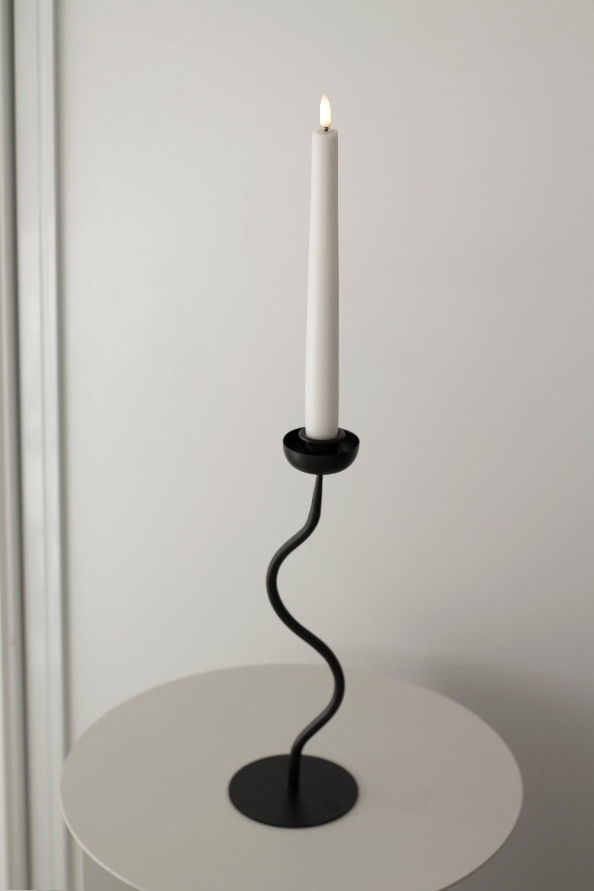 Lit white taper in the wavy black candle holder on a round white side table