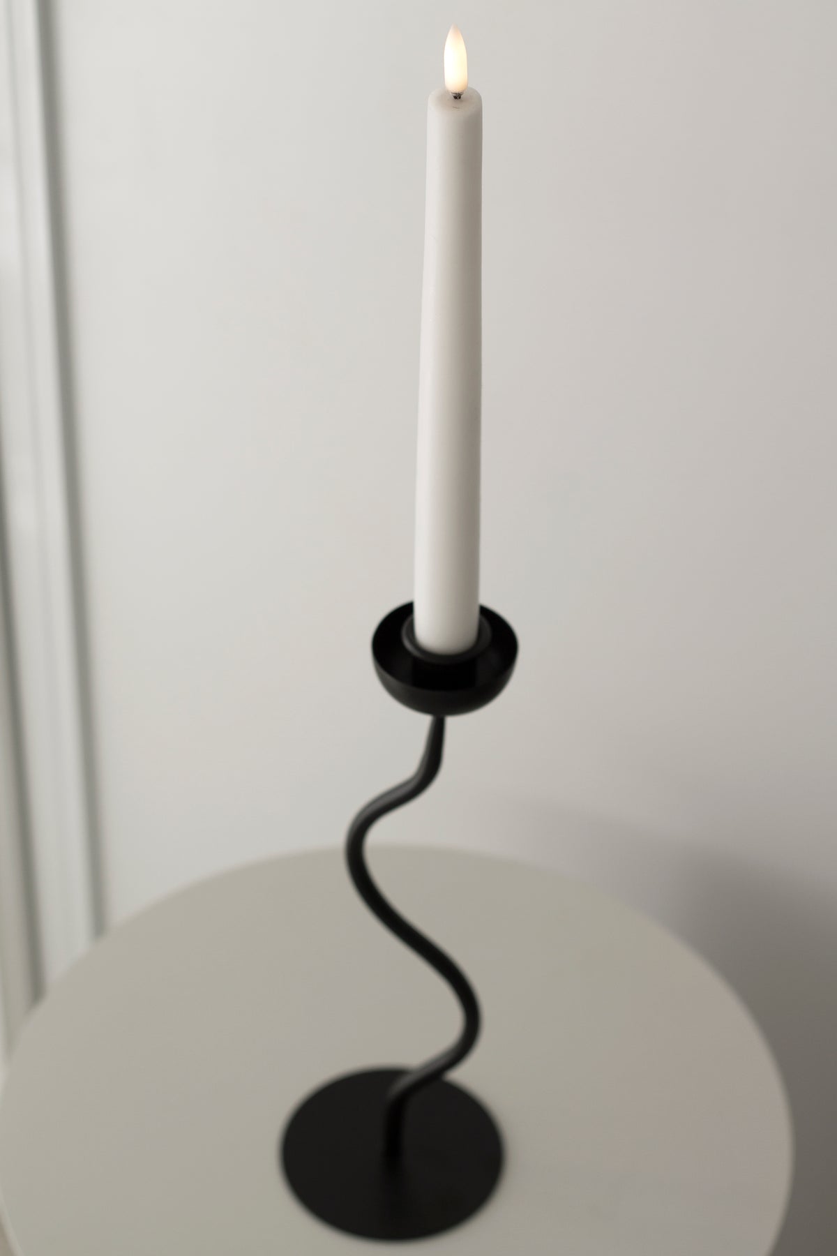 Lit taper in the Aries holder seen from a lower angle on a white table
