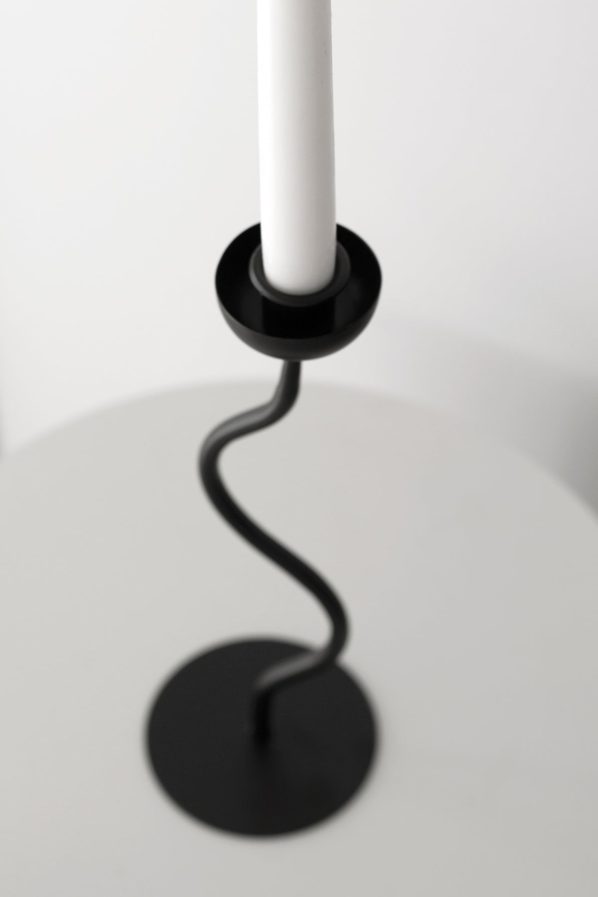Close view of the cup holding the candle base above the curving black stem