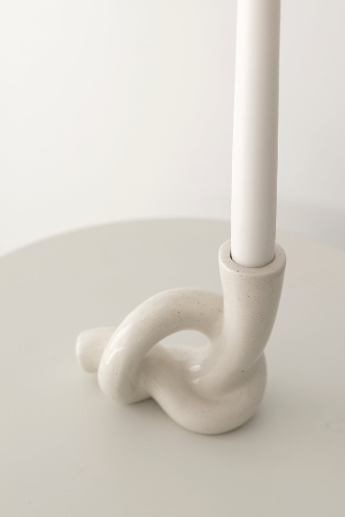 Close view of the knot holder base gripping a white taper candle on a pale round table