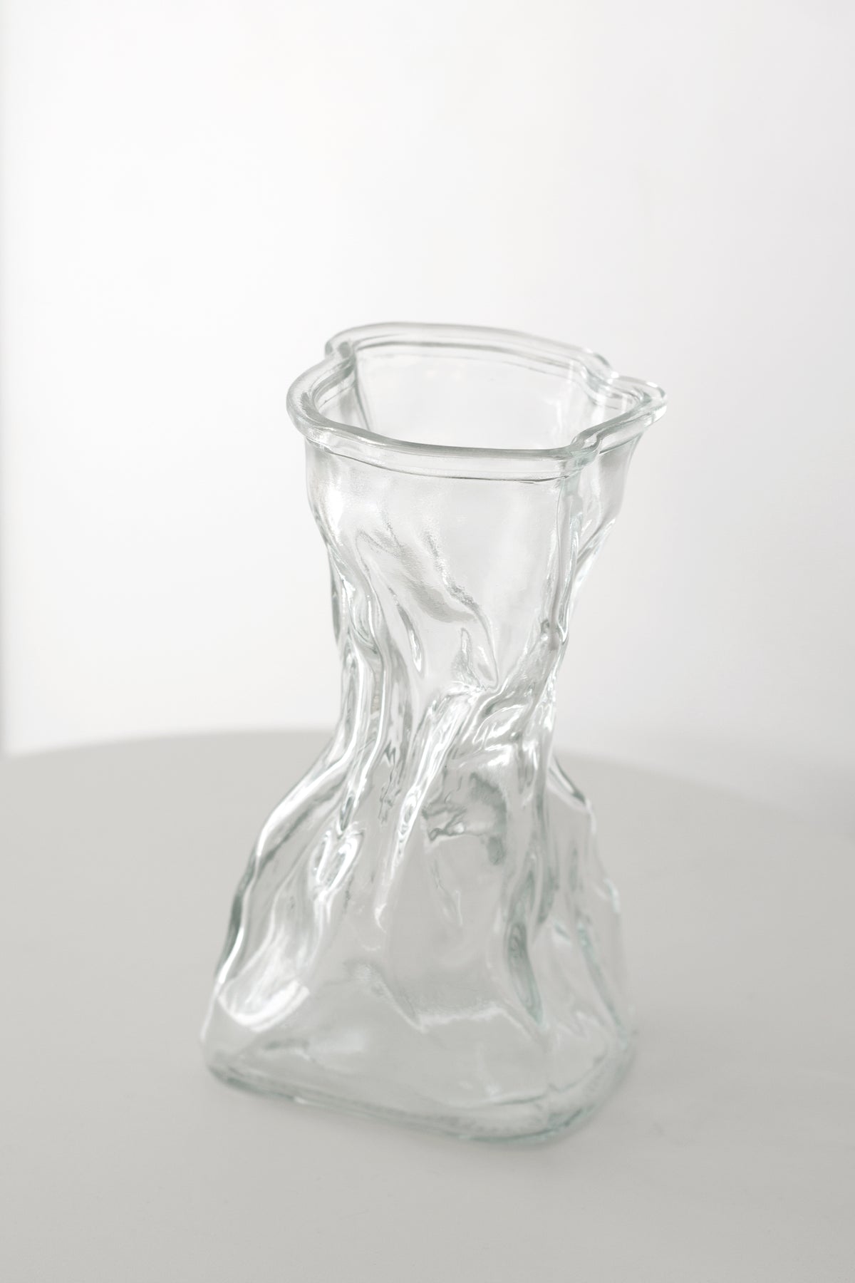 Clear crinkle vase at an angle on a round white table with bright light behind