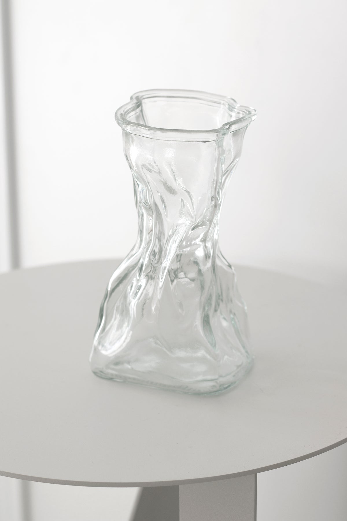 Clear crinkle vase on a round white pedestal table, framed to show the slim table base