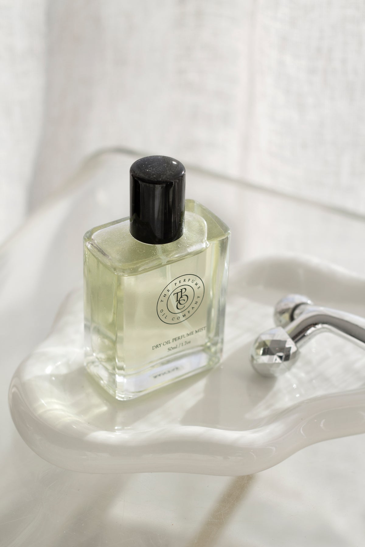 Glossy white ceramic Cloud Tray holding a dry oil perfume mist and facial roller, styled on a softly lit vanity surface.
