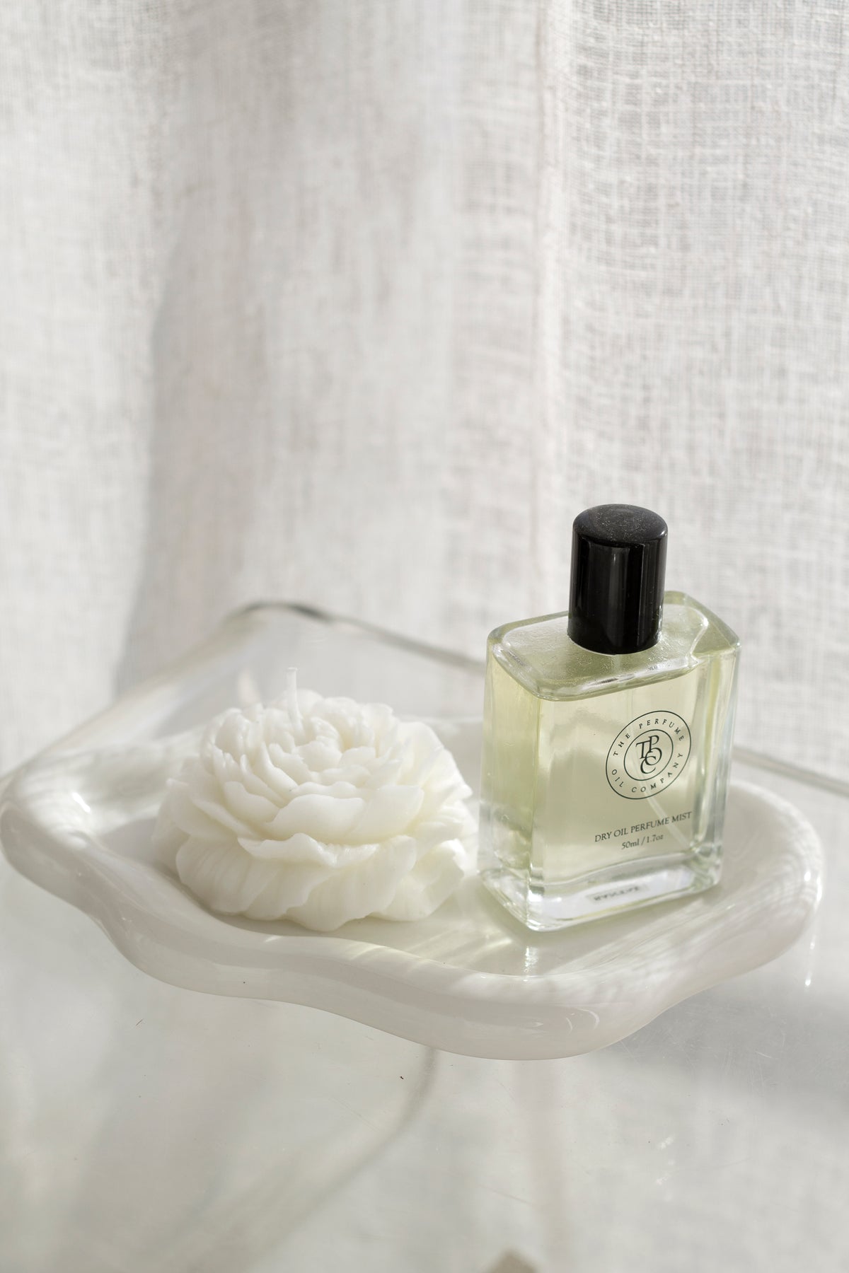 White cloud ceramic tray with a rose shaped candle and a perfume bottle on a clear table