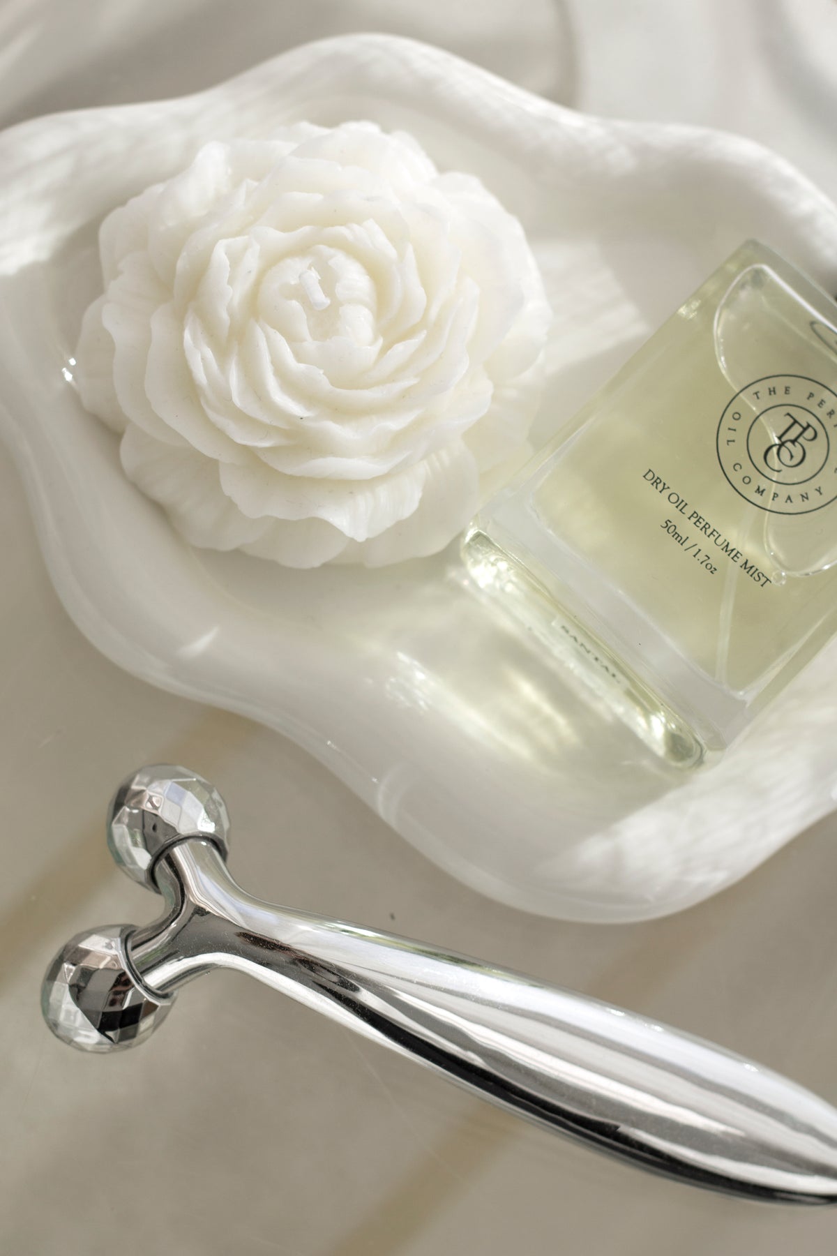 White cloud ceramic tray with a rose shaped candle and perfume bottle beside a facial roller