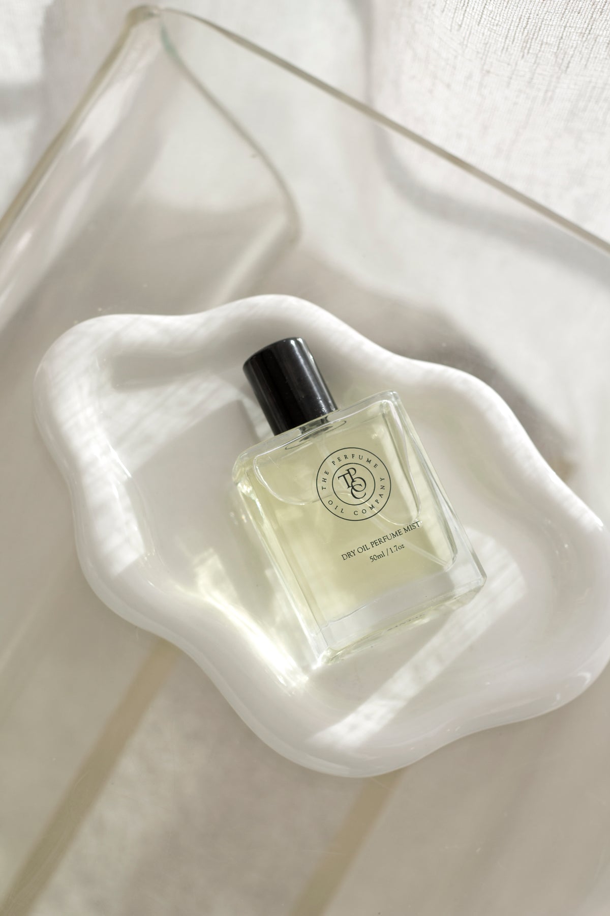 White cloud ceramic tray holding a perfume bottle against a sheer fabric backdrop
