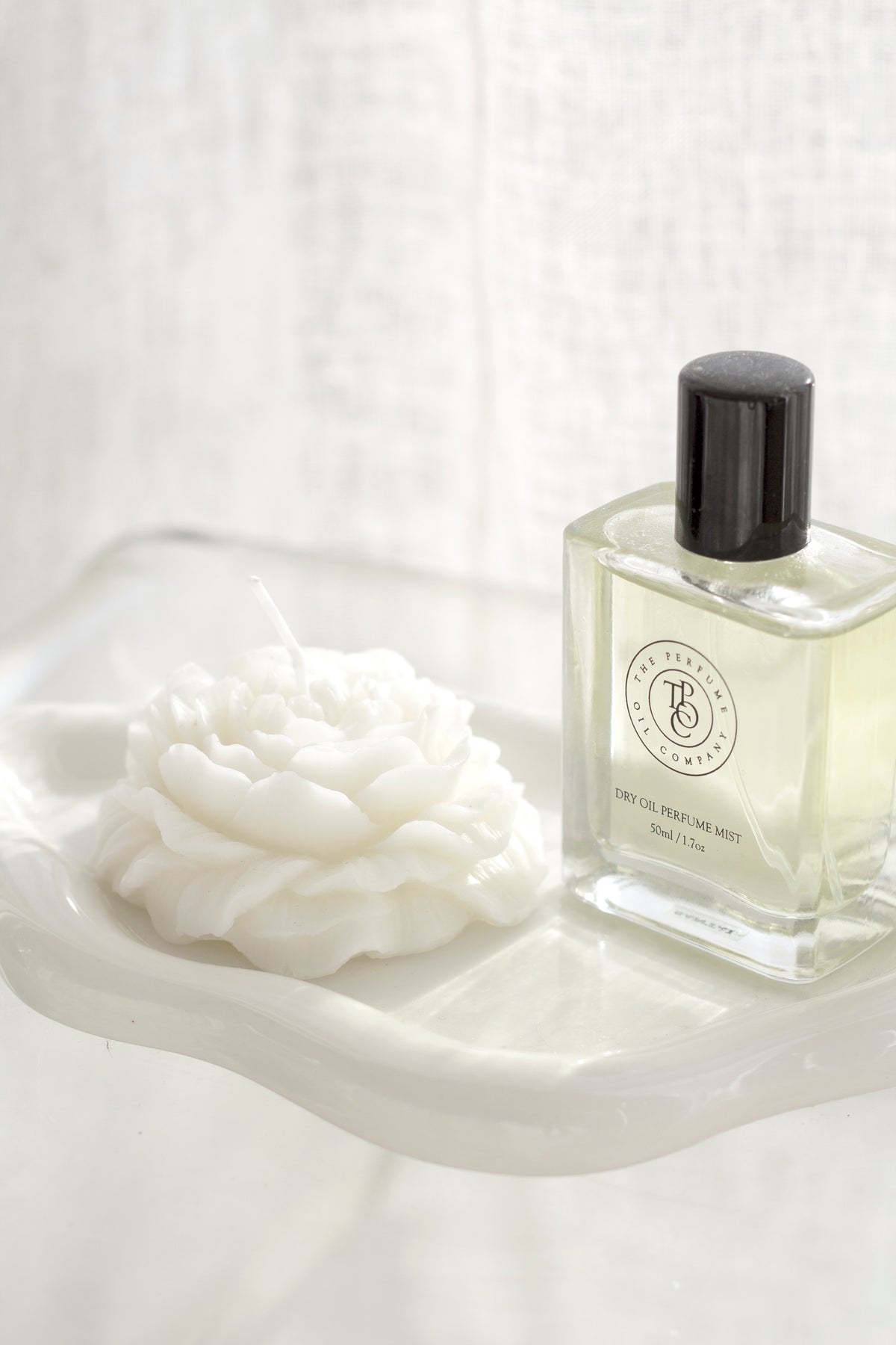White cloud ceramic tray with a rose shaped candle and perfume bottle, sheer curtain behind
