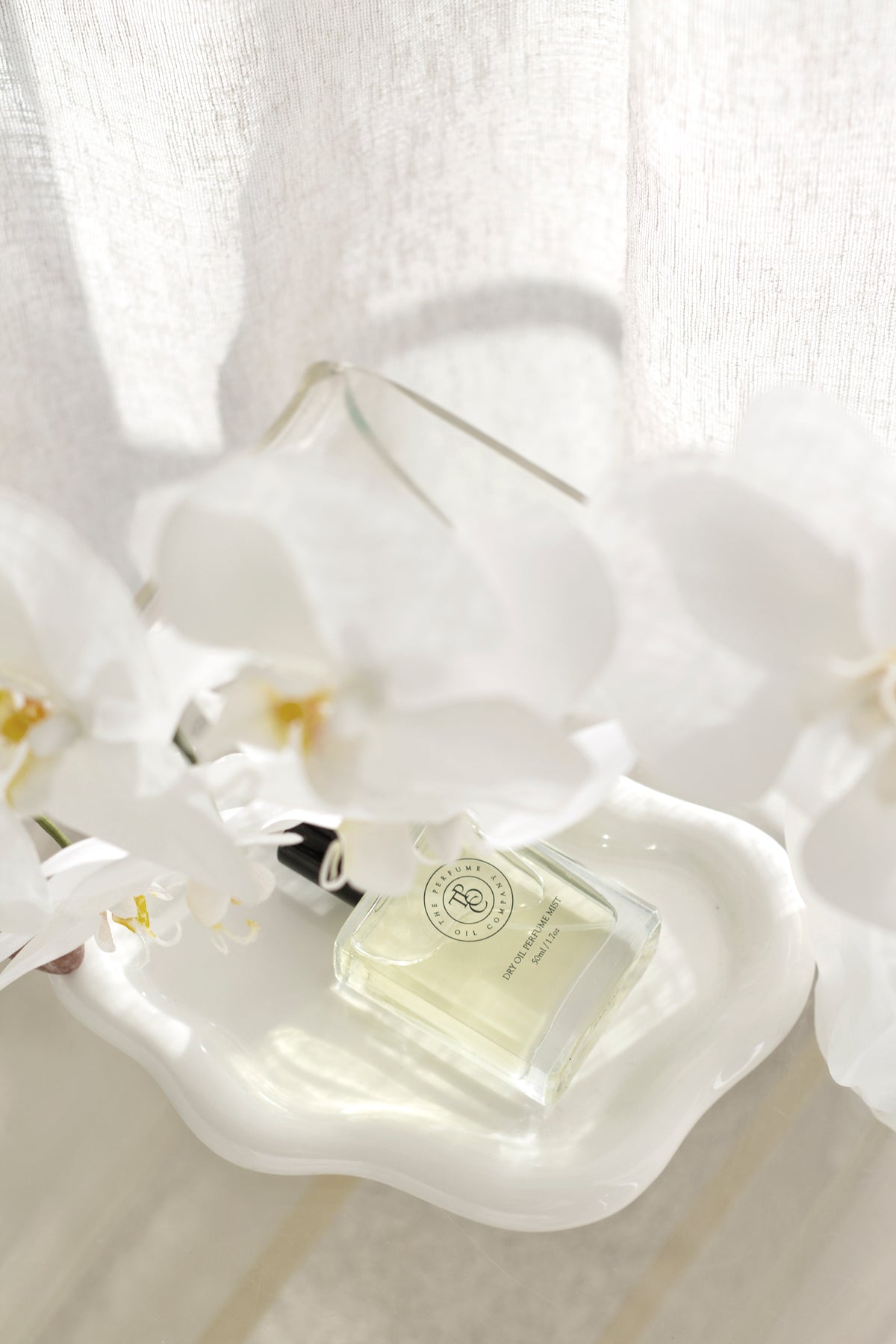 White ceramic cloud tray styled with a glass perfume bottle and white orchid flowers on a light surface.