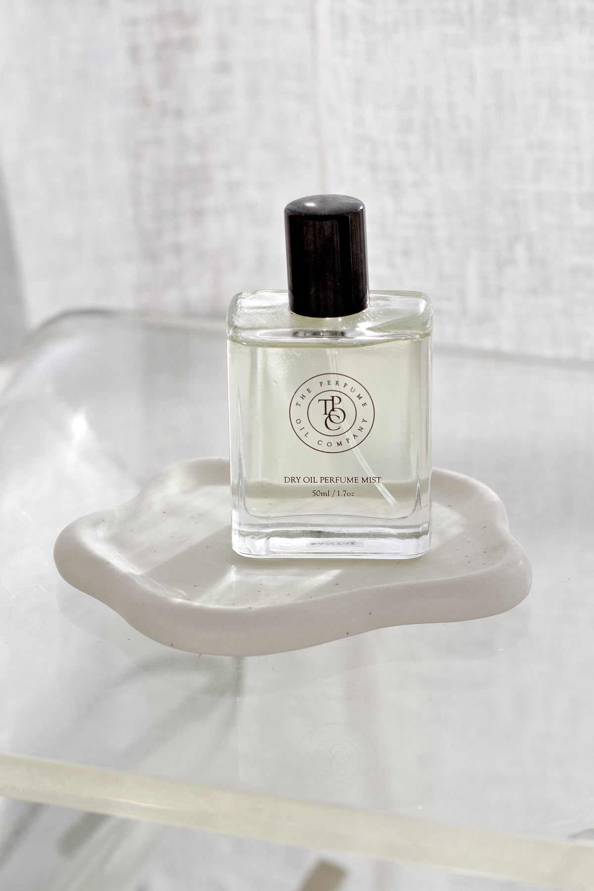 White cloud trinket dish with a perfume bottle on a clear glass table