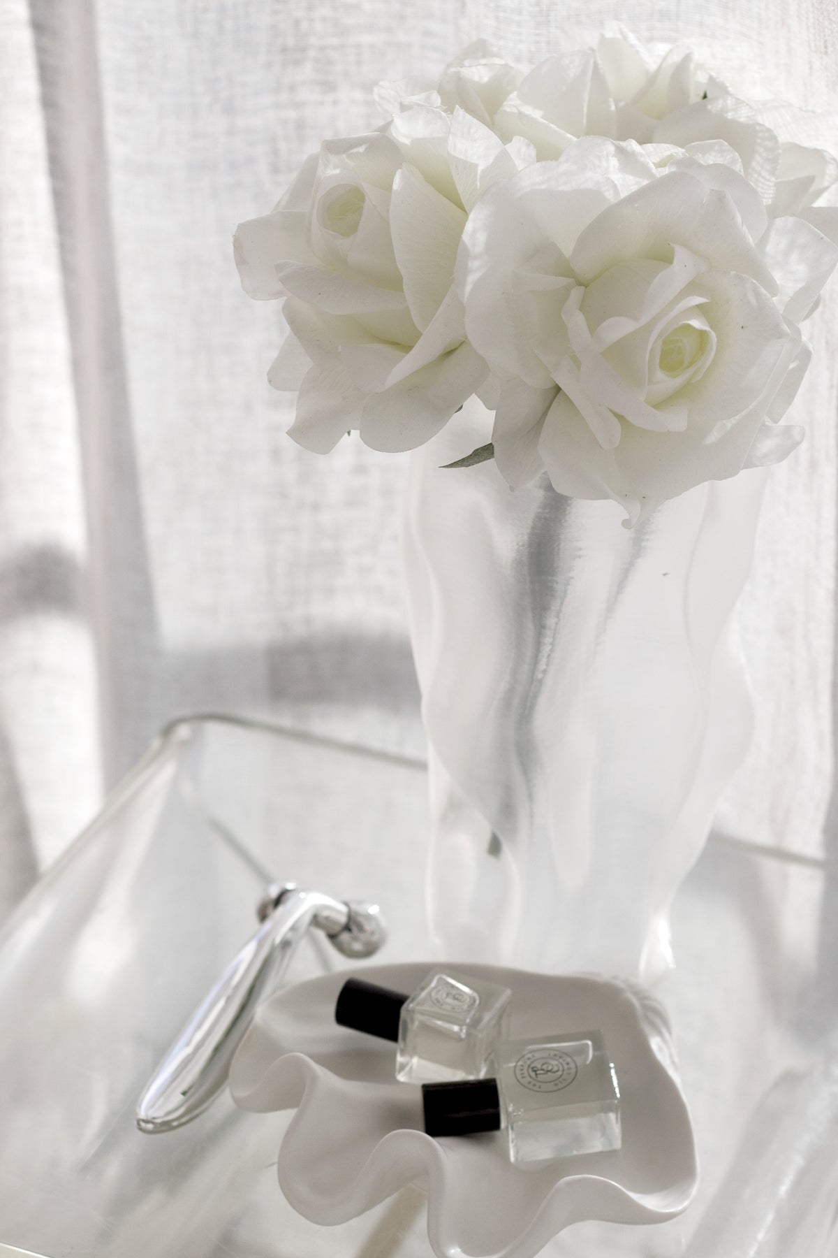 White roses in the ripple vase with two small perfume bottles resting below