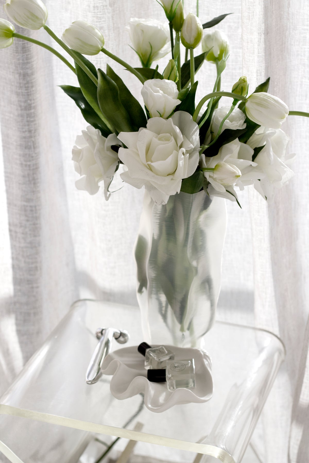 Tulips and roses filling the ripple vase on a clear acrylic table beside a linen curtain