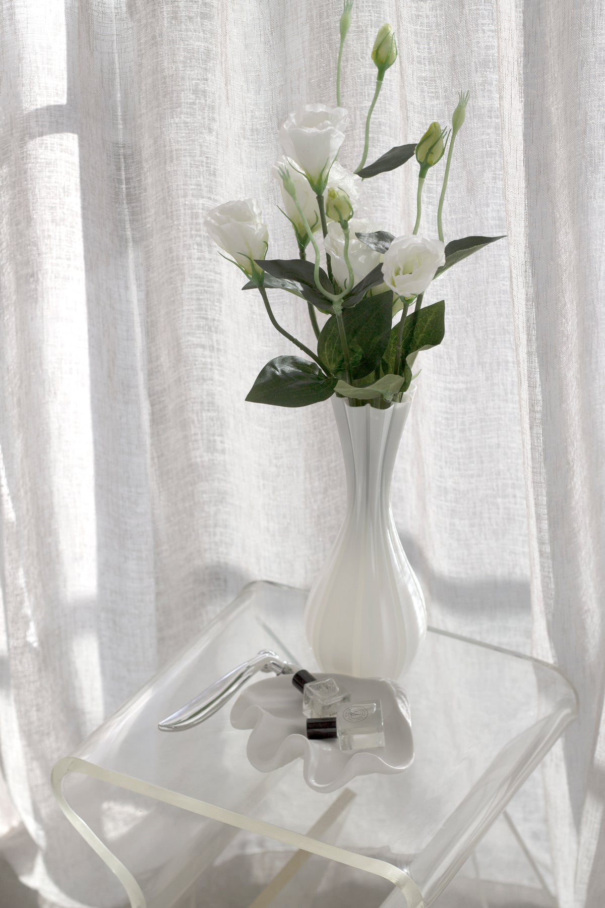 Fluted white vase holding white lisianthus on a clear acrylic side table beside a small flower-shaped dish