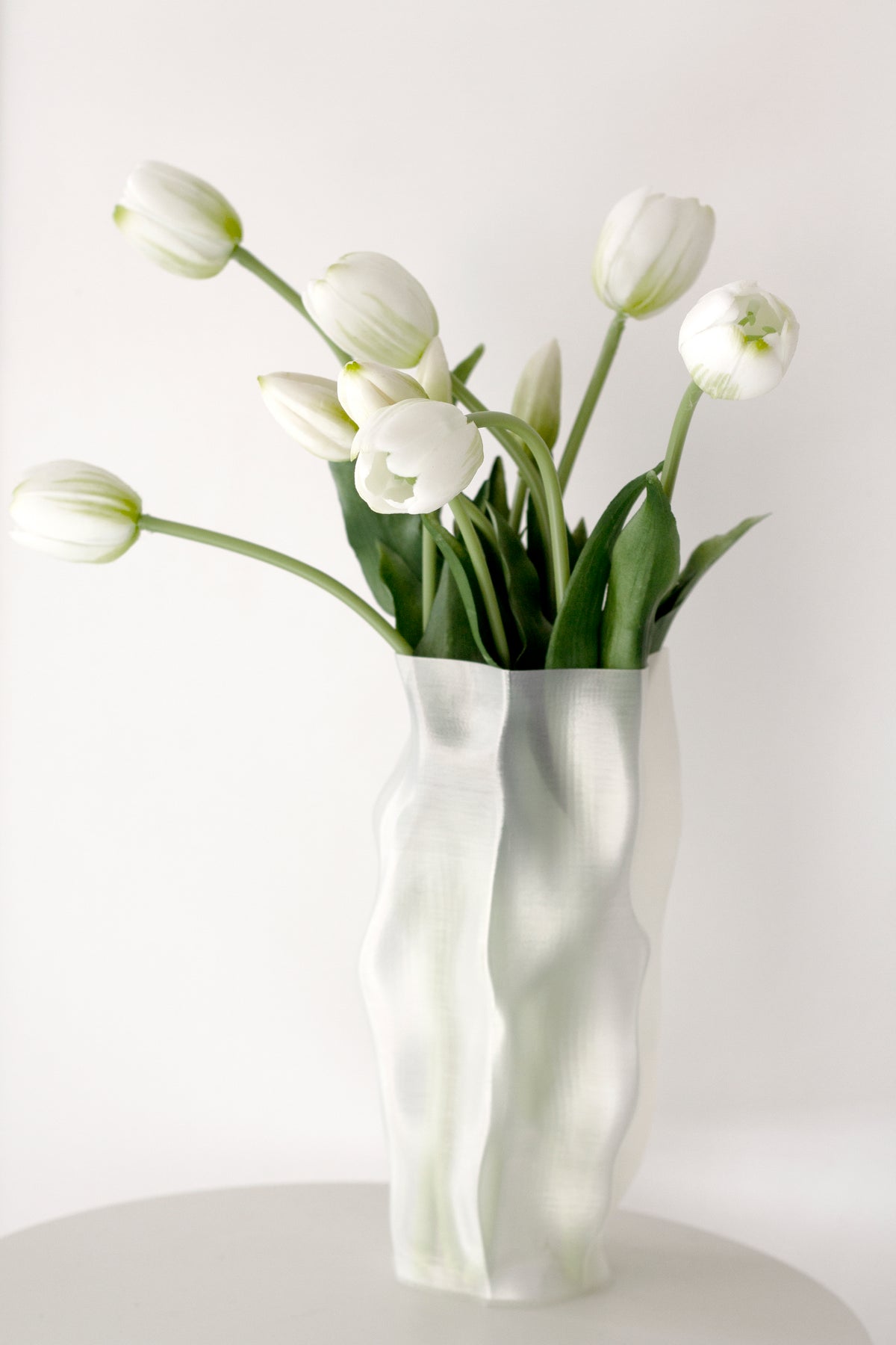 White tulips arranged in the Skyler vase on a round white table against a pale wall
